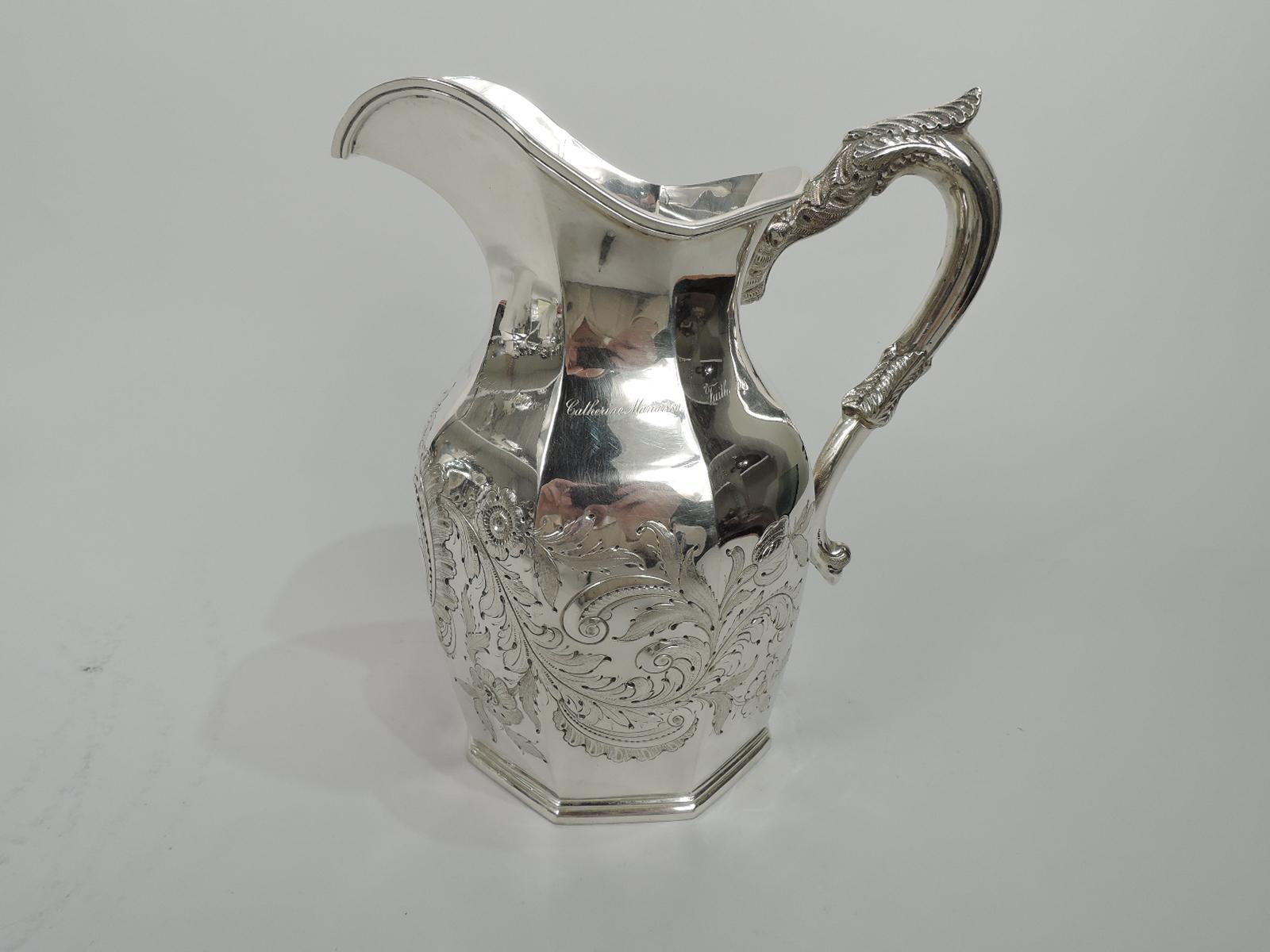 American Classical silver water pitcher. Faceted body, helmet mouth, and leaf-capped and -wrapped s-scroll handle. Chased leafing scrollwork and flowers surrounding scrolled cartouche. Engraved on front: “Made from silver tankard / brought from