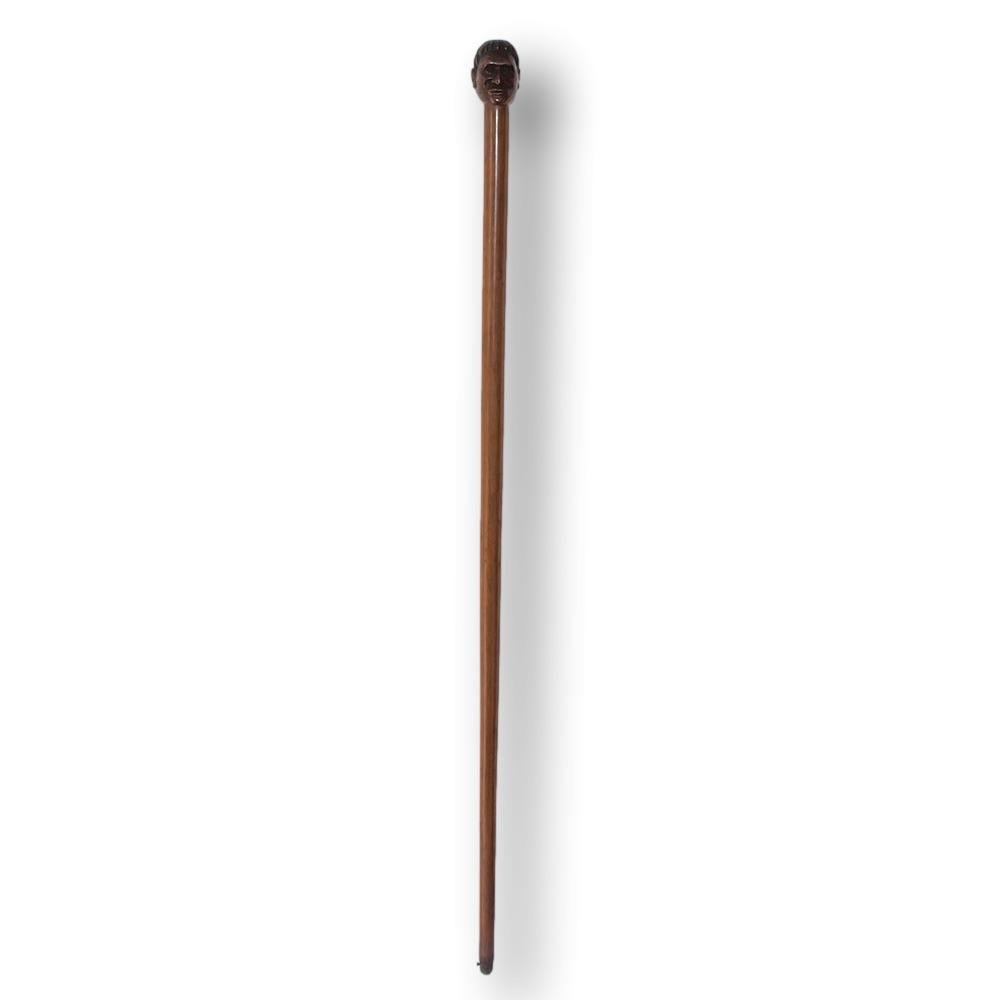 Fine and rare New Zealand Maori Tokotoko (walking stick). The cane of long tapered form with integral finial carved as a Maori chief. The figure head with Maori tattoos across face with well carved features and hair. The cane caved from one piece of