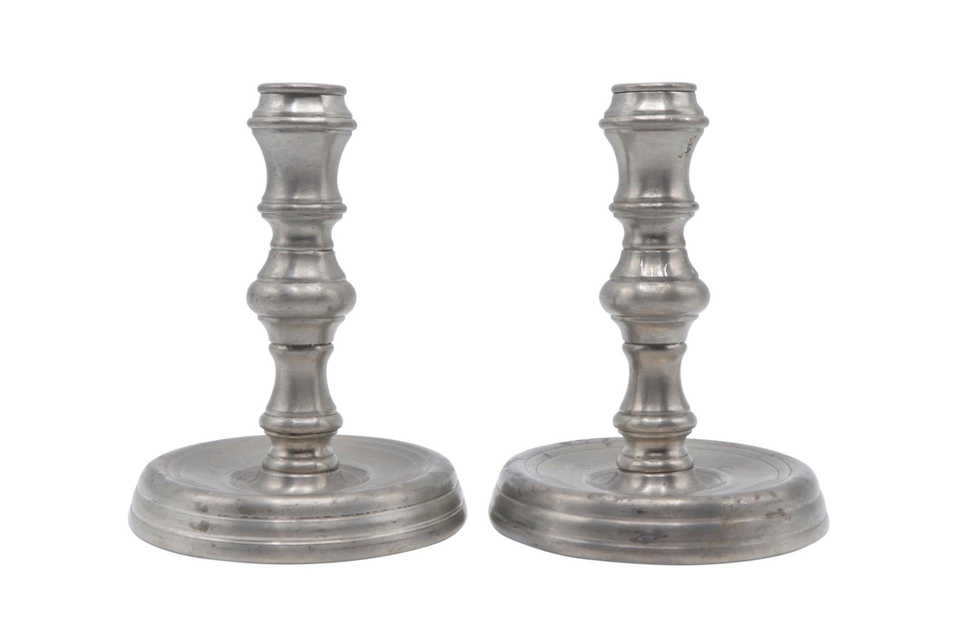 A pair of round Newburyport pewter candlesticks made by Towle. Turned columns are supported on slightly concave round bases that double as drip plates. Patina consistent with age. Dimensions per candlestick.