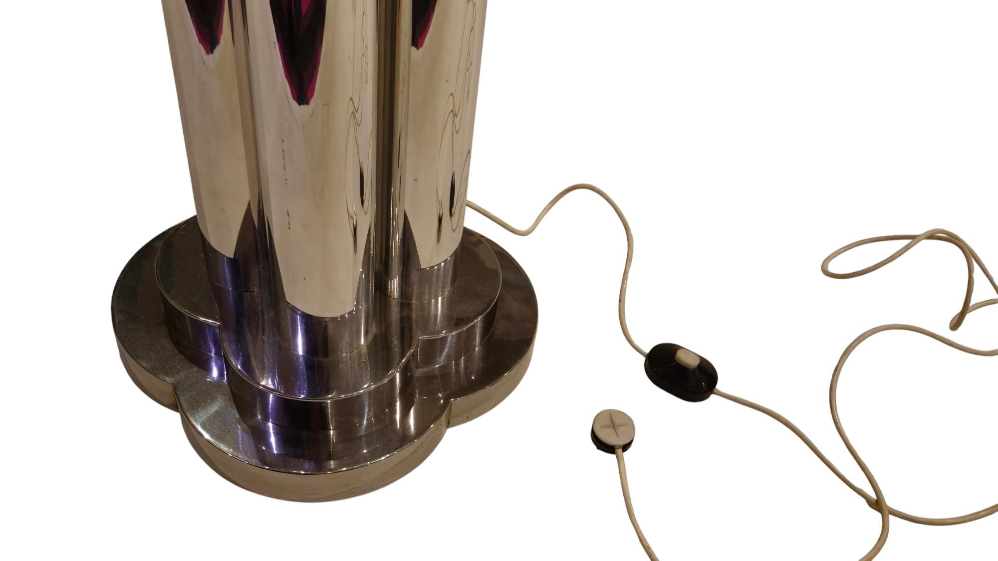 Lampada di grande impatto, una piantana alta quasi due metri, composta da quattro tubolari in acciaio che contengono un tubo in plexiglass bianco con all' interno un  unico neon originale. Nella base è contenuto lo speciale trasformatore realizzato