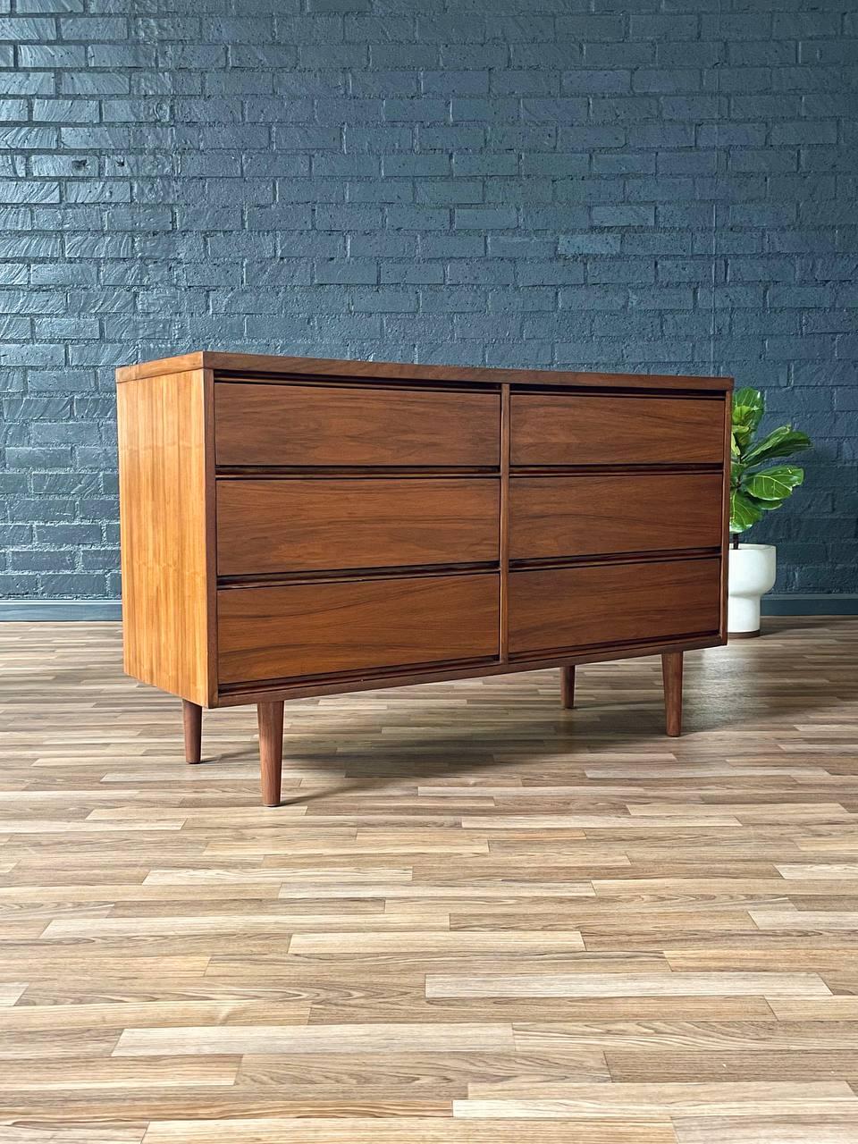 This beautifully refinished Mid-Century Modern dresser showcases timeless elegance with its clean lines and rich walnut grain. Featuring six spacious drawers, it provides ample storage while maintaining a sleek, minimalist aesthetic. The recessed