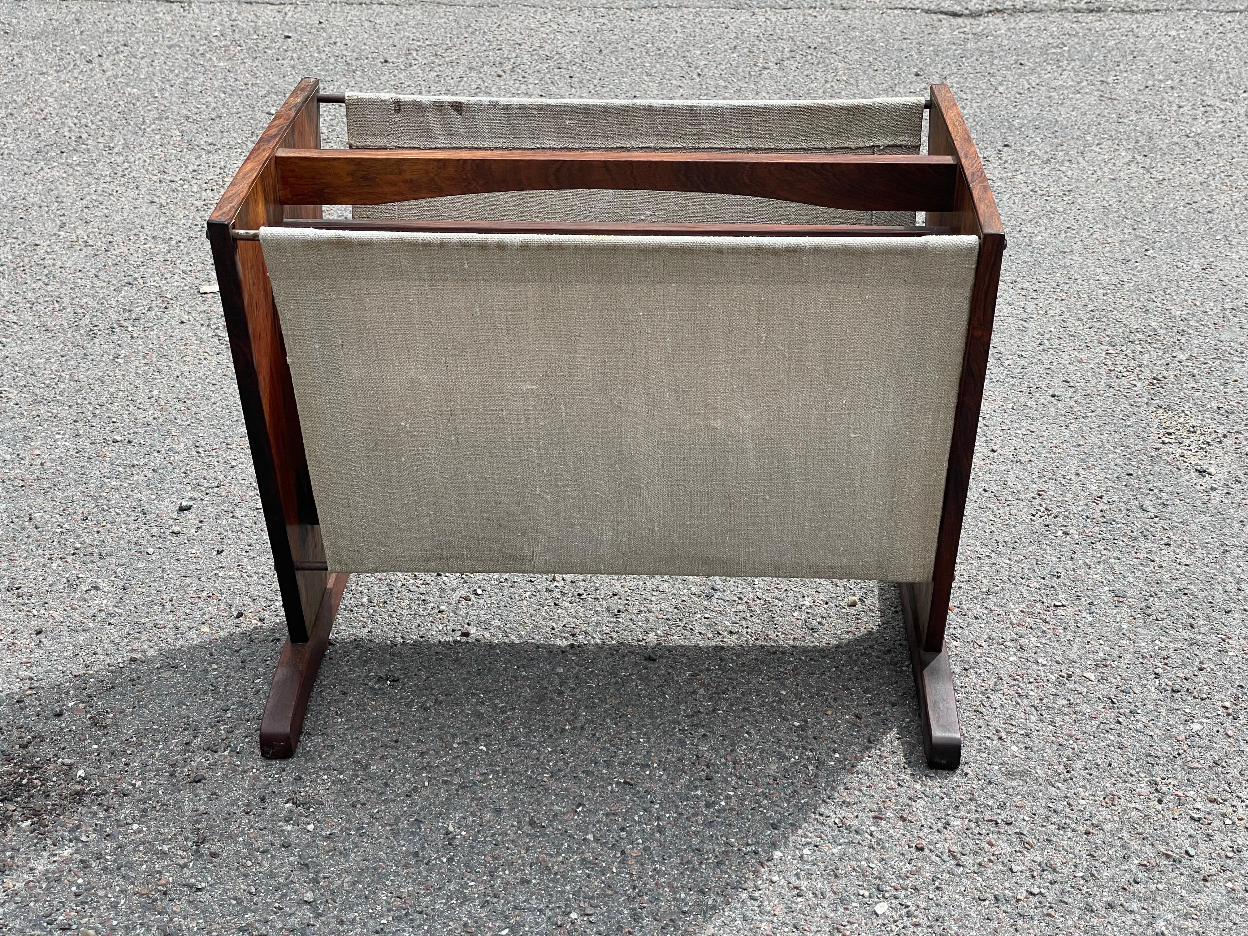 Portariviste di design danese, di squisita fattura, risalente agli anni '60. Realizzato meticolosamente in palissandro di Rio, questo pezzo emana eleganza e durata. Il tessuto ecru si abbina alla ricca patina del palissandro, creando un'armoniosa