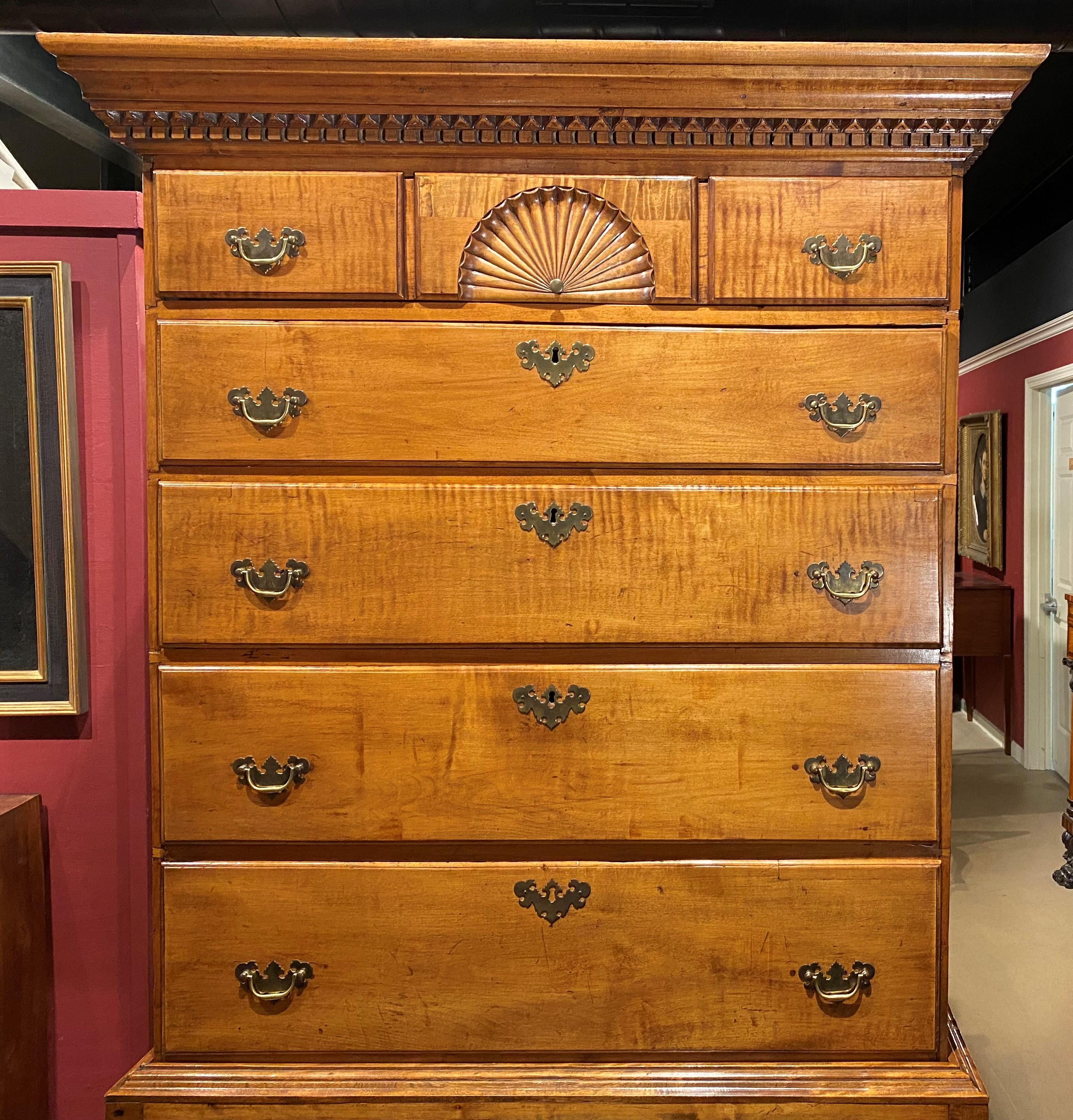 A fine example of a New Hampshire Queen Anne two part highboy in curly maple attributed to the Dunlap Workshop, circa 1760-1780, its upper case featuring a hand carved cornice with dentil molding surmounting five graduated long drawers, the top