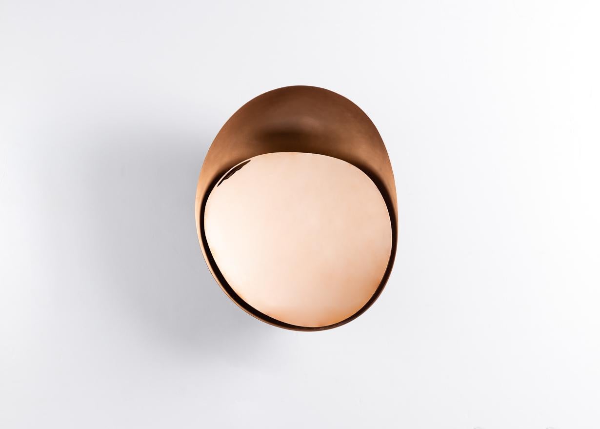 Part of the Vessel series of light sculptures, this remarkable sconce in bronze has a warm concave bowl inset with a mirror-polished shade. The misshapen ovals complement one another, not merely in their slight difference in shape and form, but in