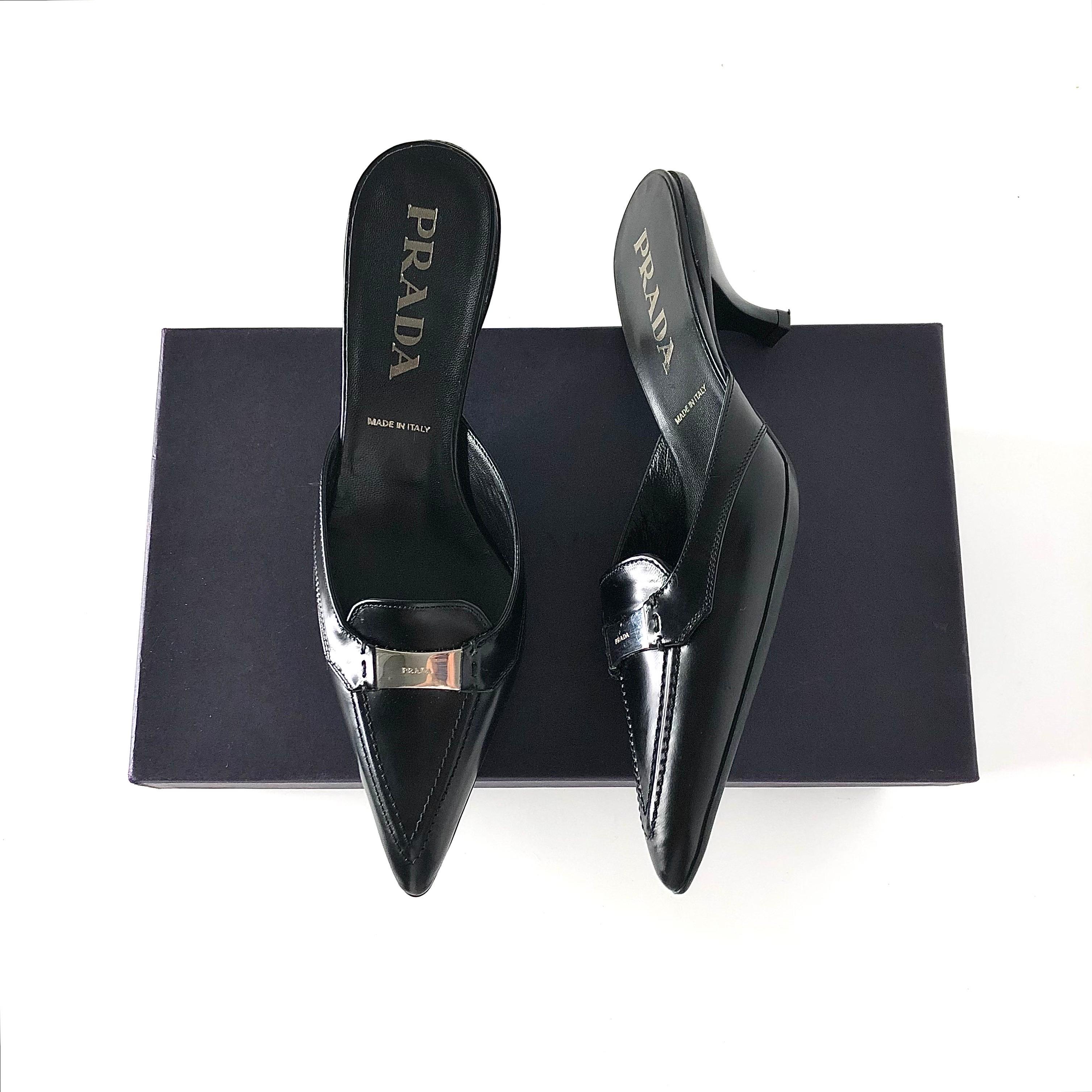 Mules con tacco a spillo con logo di Prada 
Nuovo, nella scatola originale, con sacchetto per la polvere e punte di ricambio
Colore Nero
Taglia 36.5EU
Tomaia in pelle
Suola in gomma
A punta
Tacco basso
Abbellimento con logo a placca
Tacco di 2