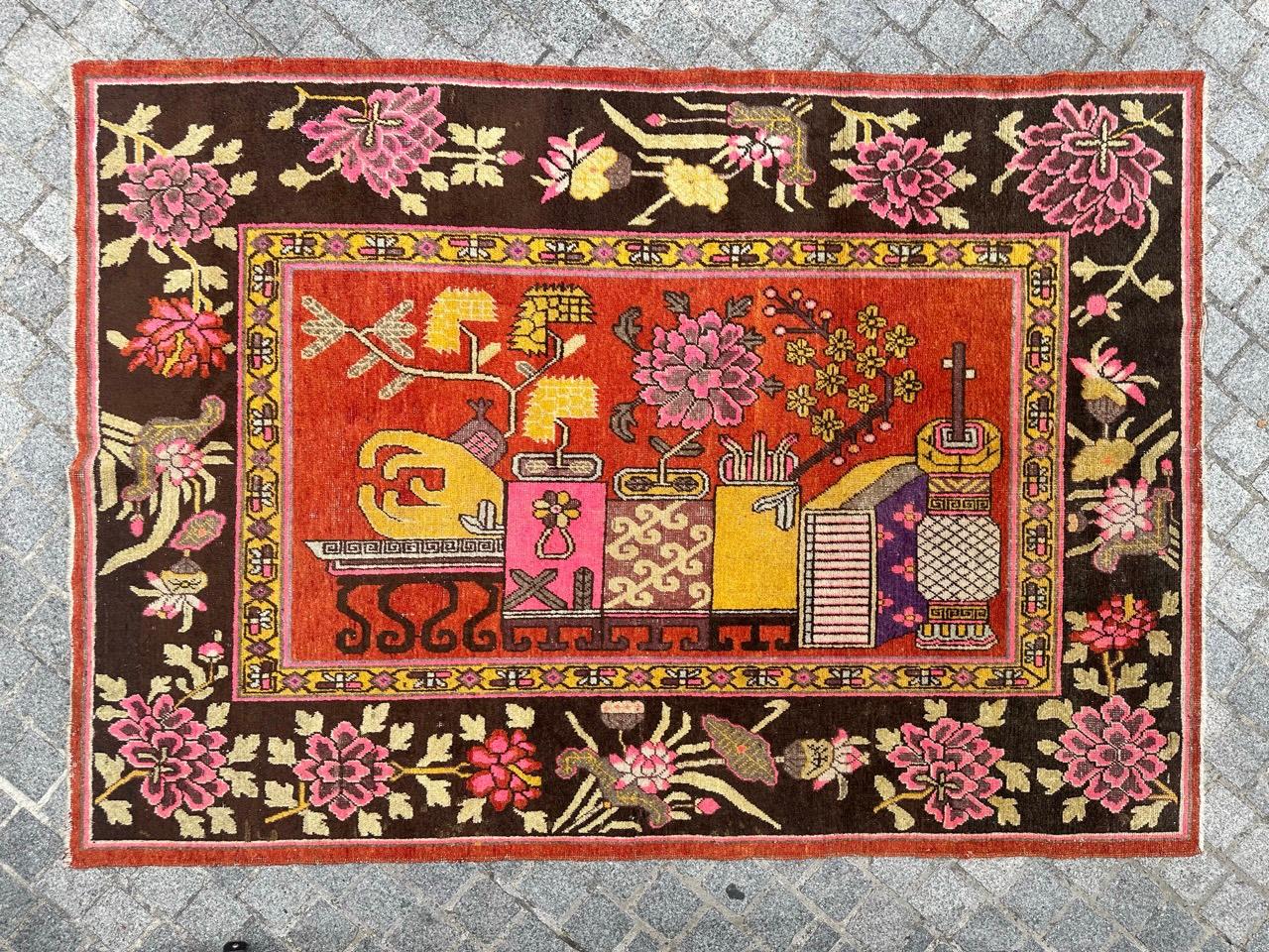 Exquisite Chinese Khotan Rug with Central Figurative Design and Floral Vases. There’s a decorative stool, adorned with vases of flowers in shades of pink, yellow, violet, brown, and beige. The stylized vases exhibit matching colors, including
