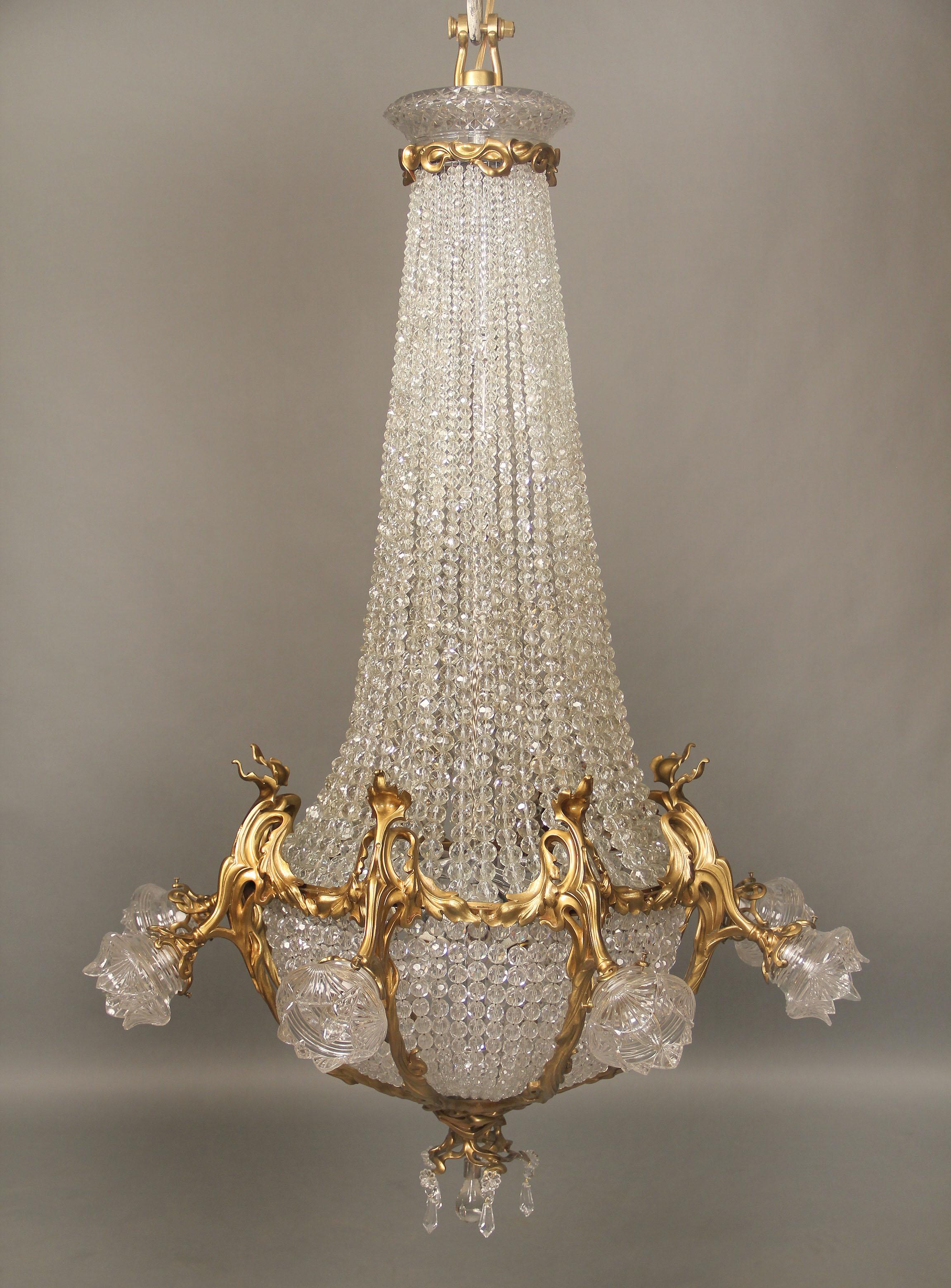 A nice early 20th century gilt bronze and crystal sixteen-light basket chandelier

The cut crystal top with a gilt bronze rim, beaded strings run down to the basket, the base with a crystal bulb and drop crystals, eight perimeter bronze arms with