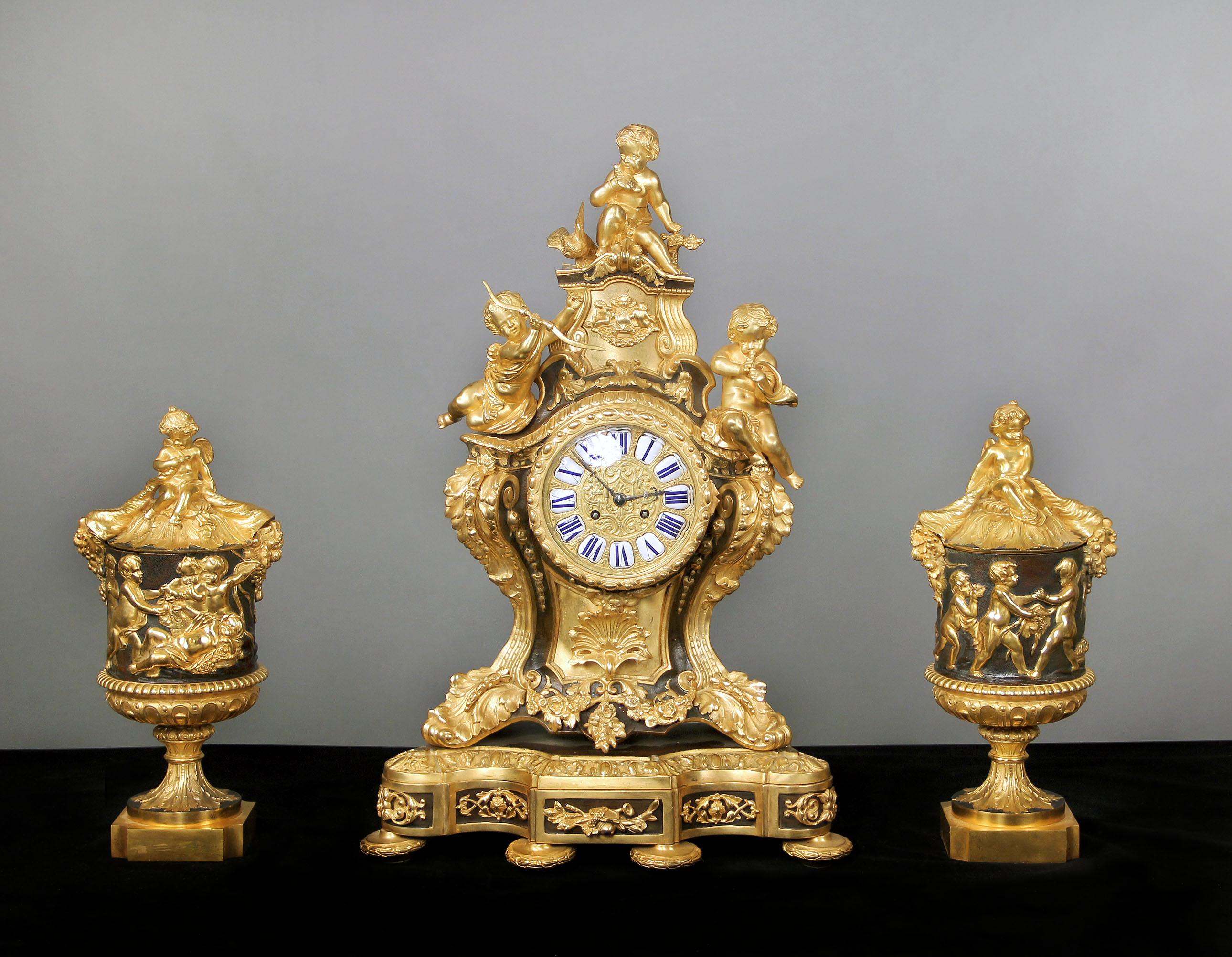 A nice late 19th century gilt and patinated bronze three-piece clock set.

The heavily bronze mounted clock with three putti, bronze designs of flowers, birds and instruments, sitting on a base. The urns with central Bacchanalian frieze topped