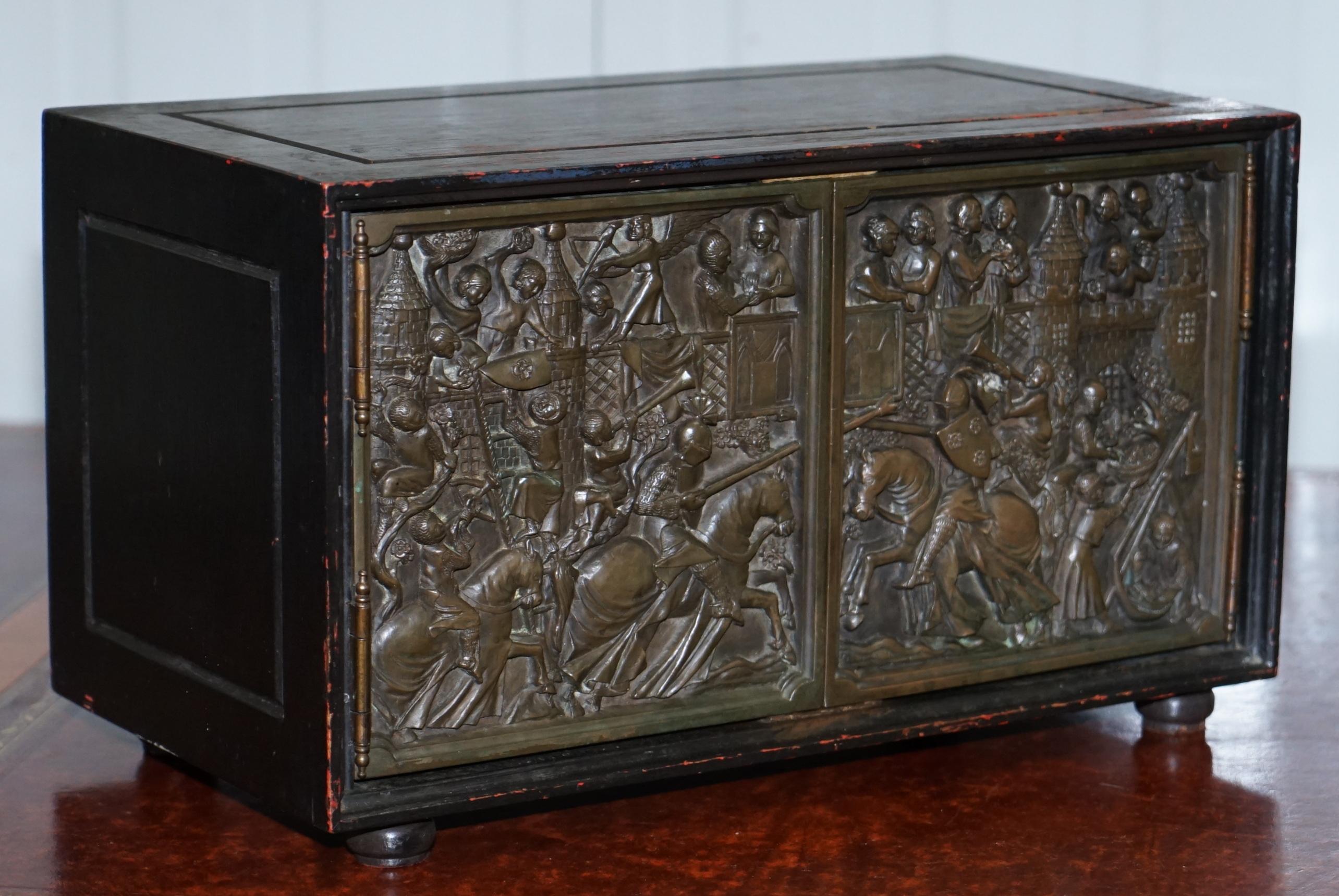 We are delighted to offer for sale this lovely small cabinet with Bronze doors depicting a jousting tournament

A good looking and very decorative little table top cupboard with very nicely cast bronze doors

We have lightly cleaned waxed and