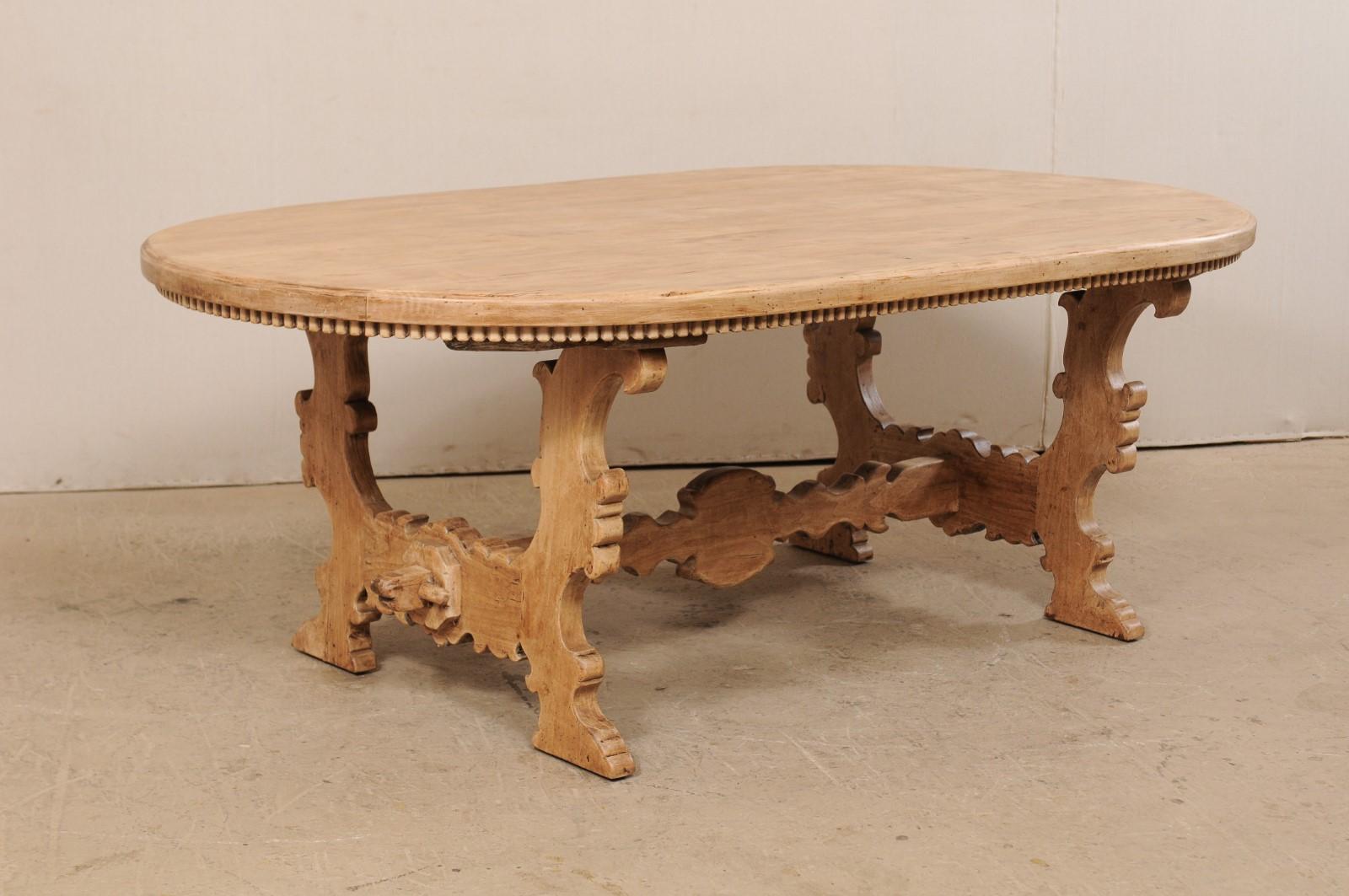 A vintage Italian-style American oval-shaped table trestle table. This shapely dining table features a 7 foot long oval-shaped top, and has an Italian inspired design with curvaceous carved lyre shaped trestle legs in a leaf-motif, with center