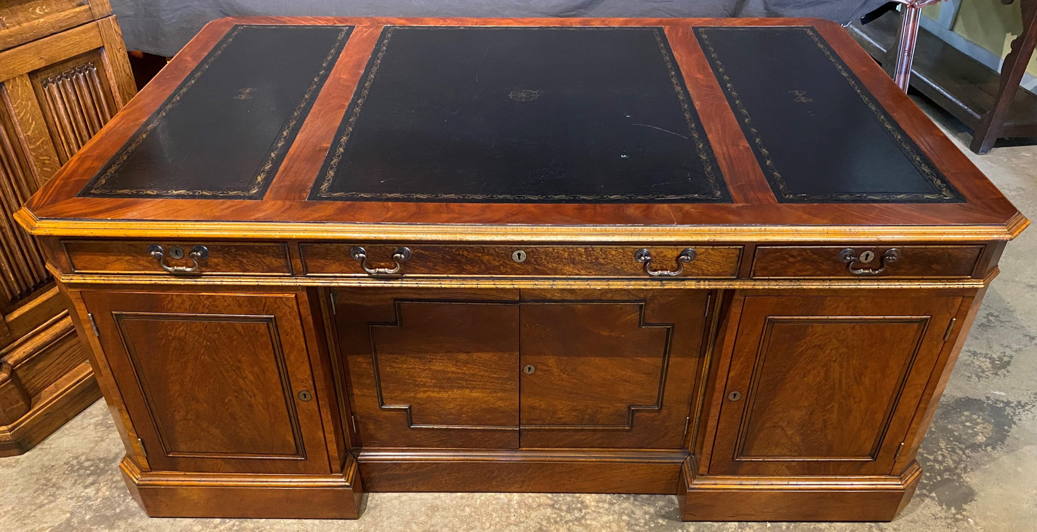 A fine mahogany and burled walnut veneered partners desk with three section tooled black leather top with molded edge and canted corners, with three fitted front frieze drawers over a two paneled door center front storage compartment flanked by