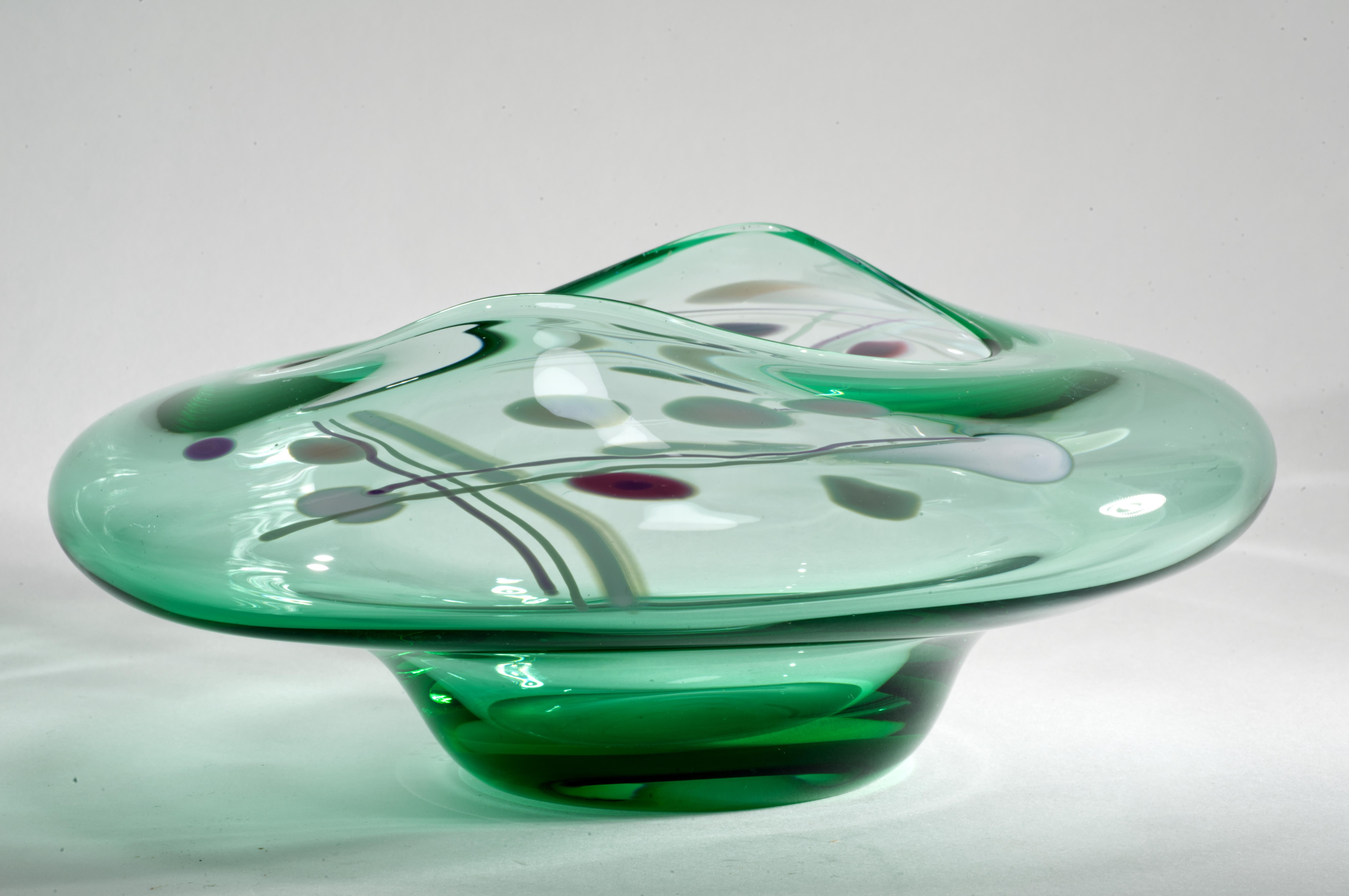  Die biomorphe Vintage-Glasschale wurde 1992 von Rick und Janet Nickolson entworfen. Sie zeigt zwei abstrakte Muster aus rosa, cremefarbenem und weißem Glas, die auf einem dünnen, fast transparenten grünen Glasgrund aufgeschmolzen sind. Die grüne