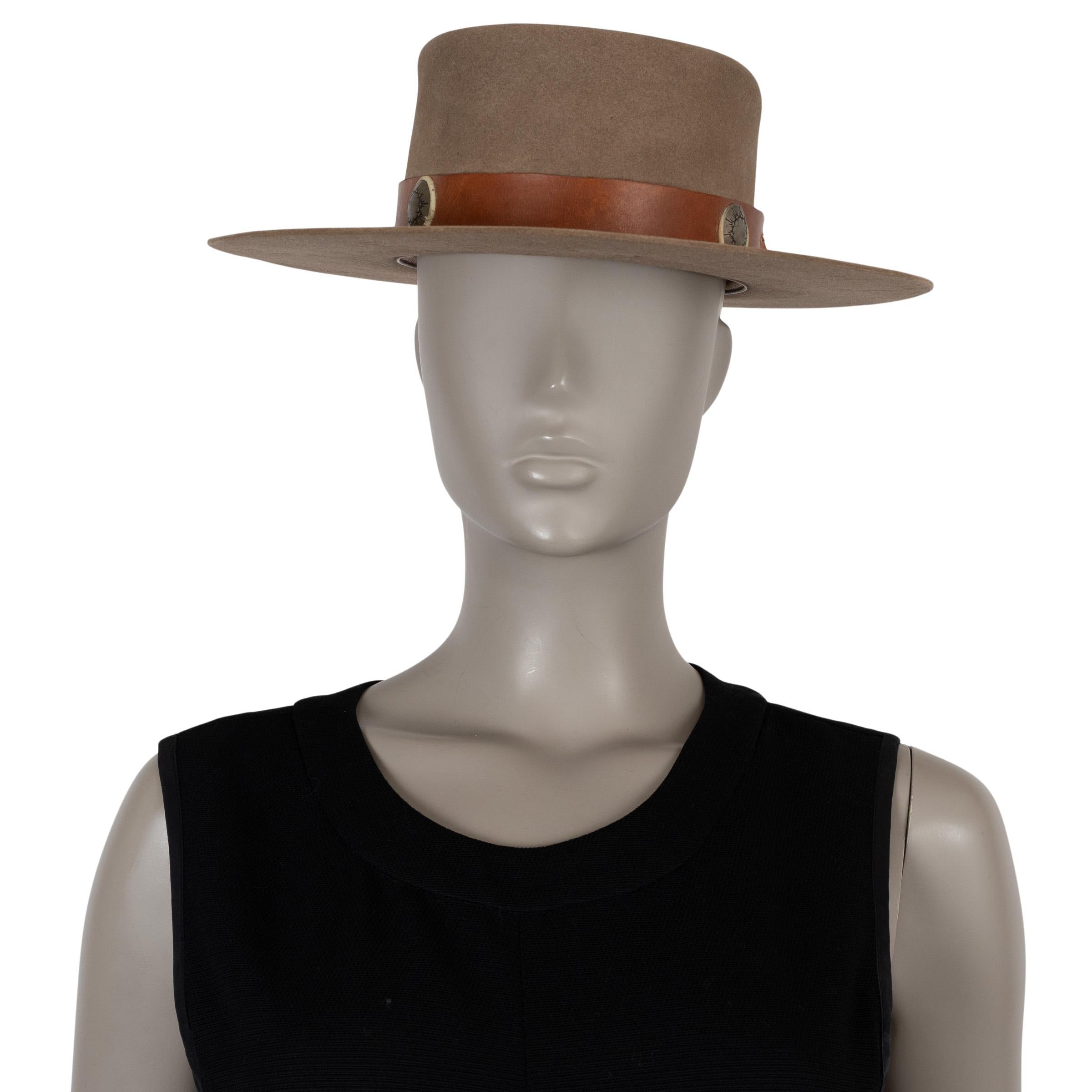 Questo cappello fedora Nick Fouquet 279, autentico al 100%, è realizzato in feltro di castoro color tortora (100%). Presenta una silhouette strutturata a fedora con una tesa larga e una fascia in pelle marrone, ornata da medaglioni di monete in
