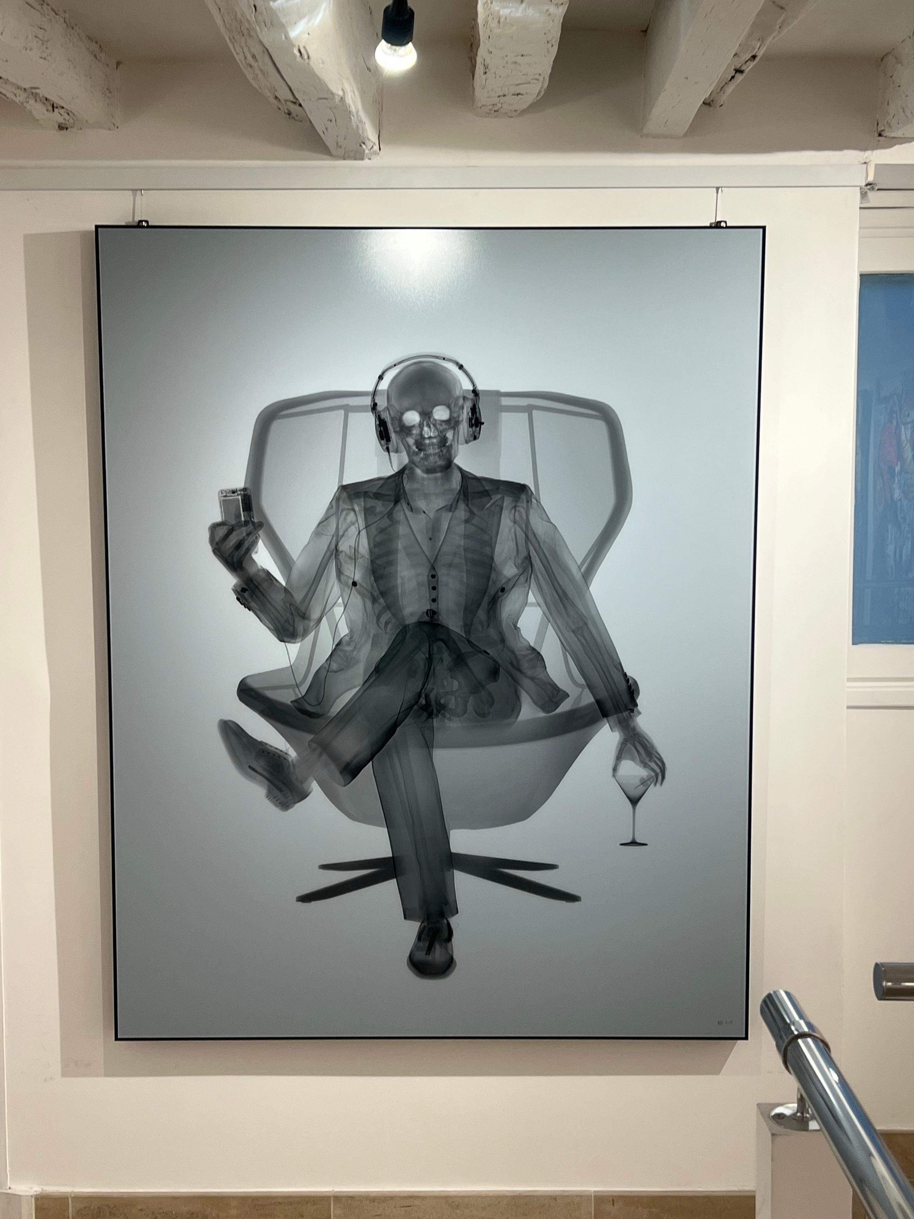 Eine Originalfotografie, in großer Auflage von 9 Stück. 
Signiert und nummeriert 2 von 9.
Verkauft gerahmt und begleitet von der COA des Künstlers.

Dieses faszinierende Kunstwerk zeigt eine skelettierte Figur, die elegant in einem modernen Sessel
