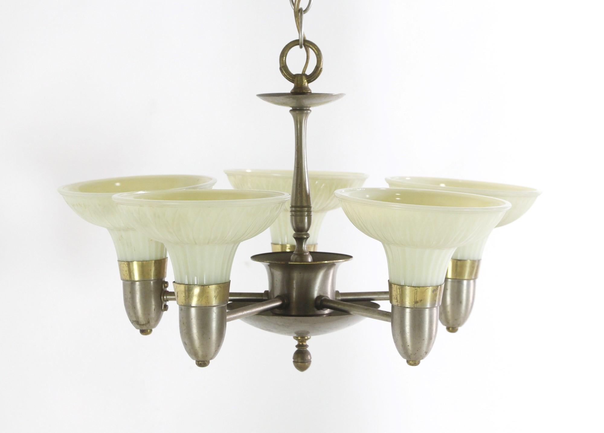 Mid 20th century chandelier done in an Art Deco style featuring a brushed nickel and brass finish with five arms and white embossed glass shades. Minor bends and minor chipping. Please see the photos. This can be seen at our 400 Gilligan St location