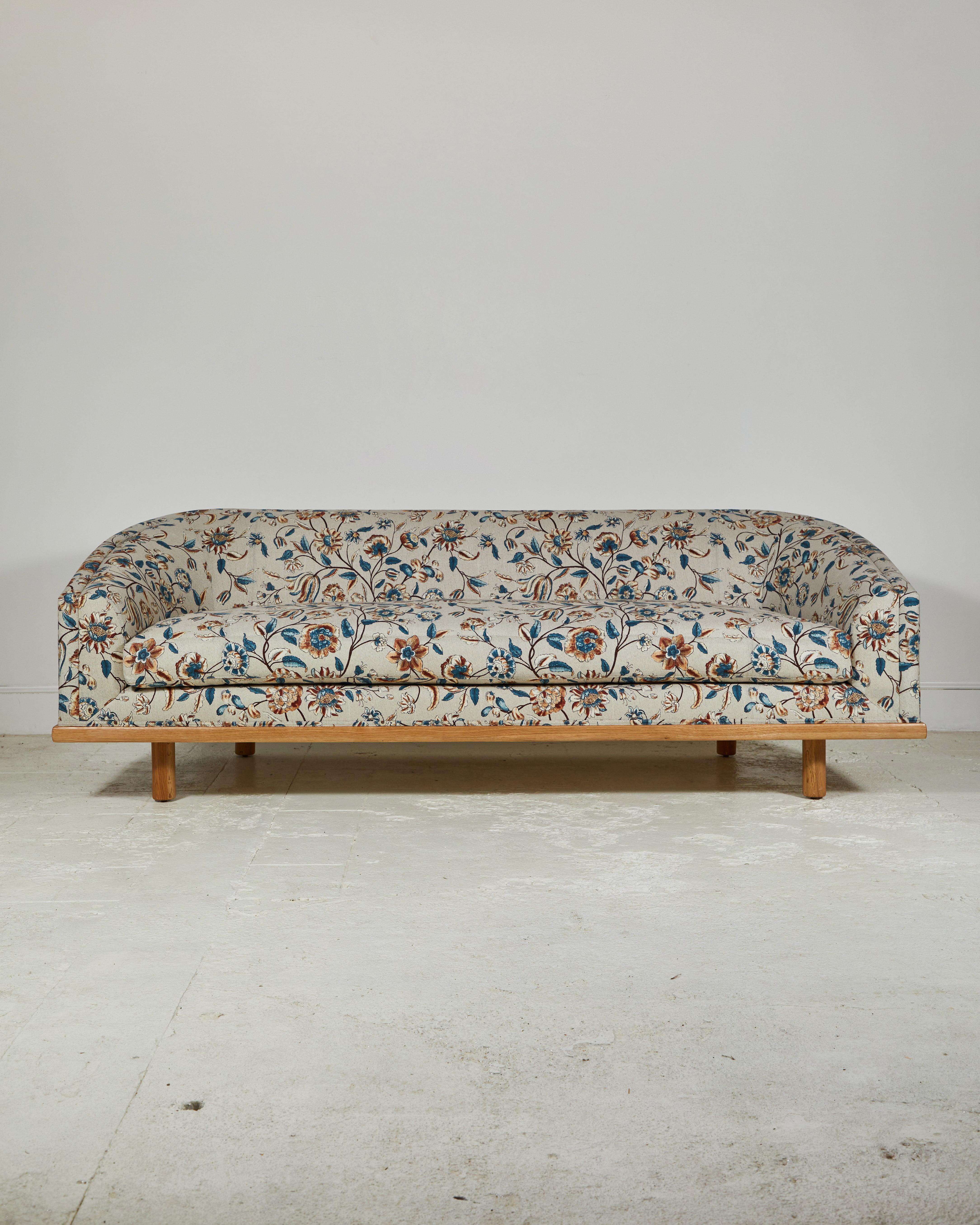 Elegant tight back sofa with curved silhouette and delicious depth. Long single seat down/feather cushion wrapping foam core, set on solid walnut framed-base atop Classic minimal cylinder legs.

This specific sofa is upholstered in floral fabric
