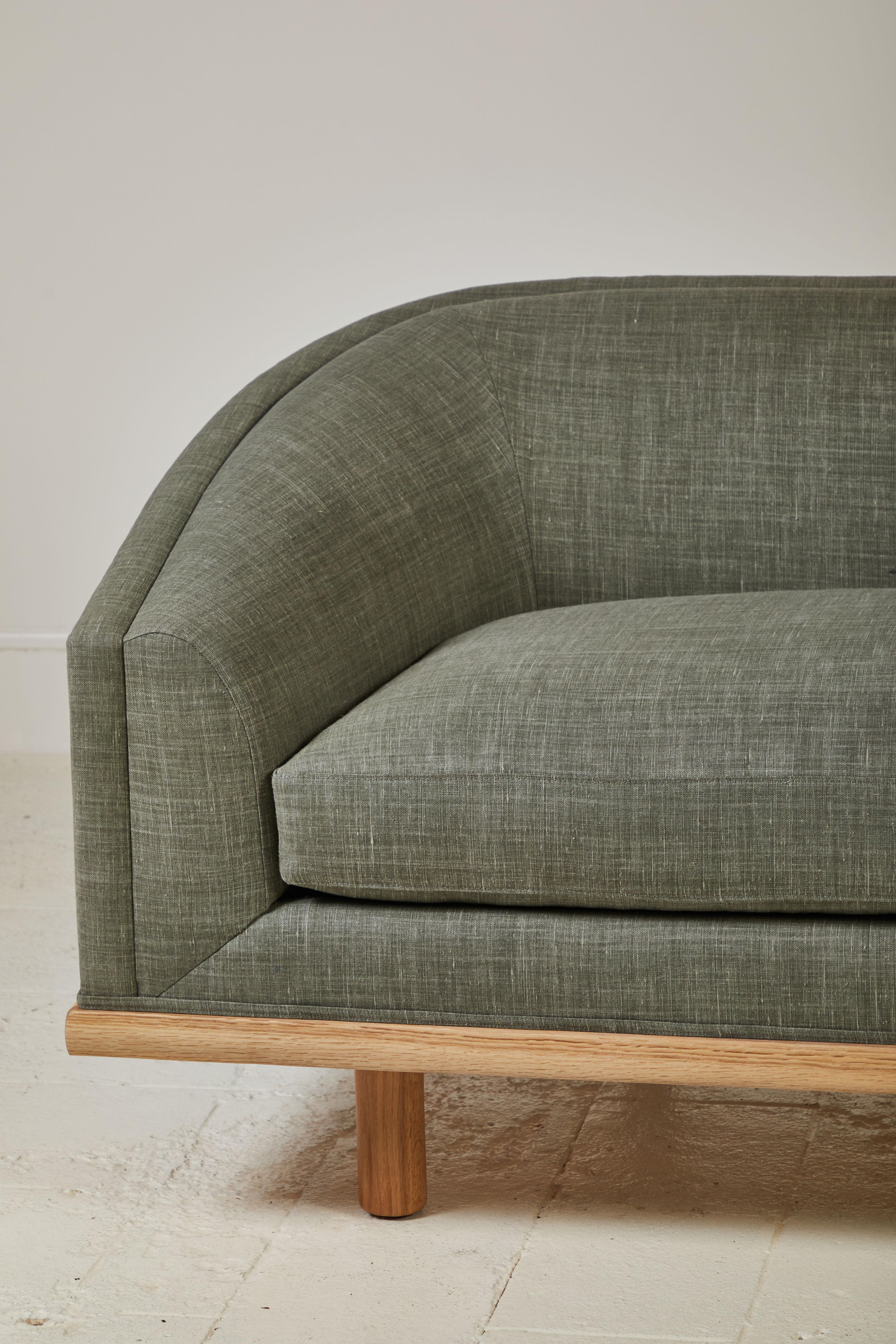 Elegant tight back sofa with curved silhouette and delicious depth. Long single seat down/feather cushion wrapping foam core, set on solid walnut framed-base atop Classic minimal cylinder legs. This specific sofa is upholstered in a dune green linen.