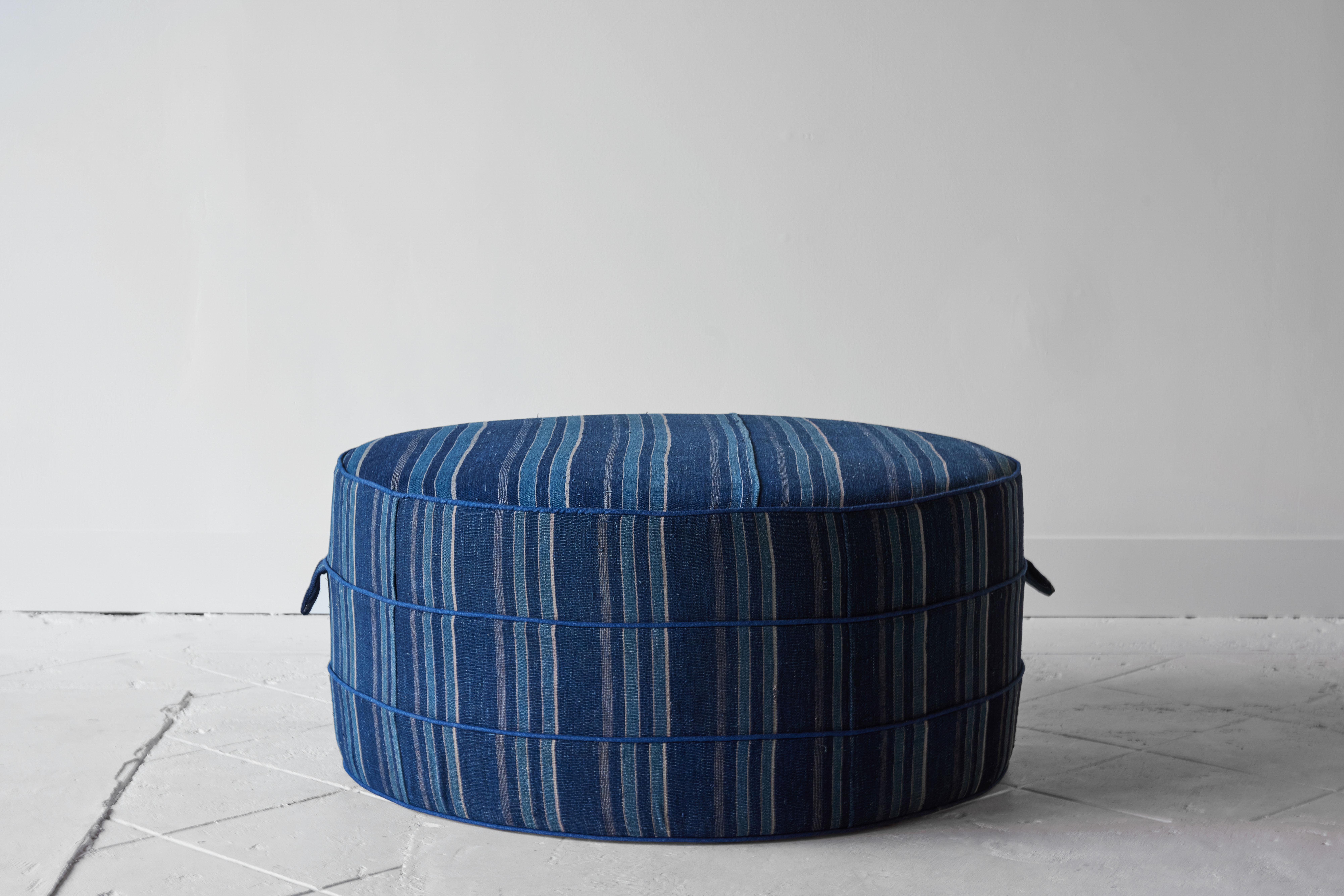 Our large round hassock upholstered in a beautiful indigo textile handwoven by the Dogon tribe in Mali, Burkina Faso, Africa is the perfect addition to any room. Solid wood frame and upholstered hassock with two ring piping and double handle details