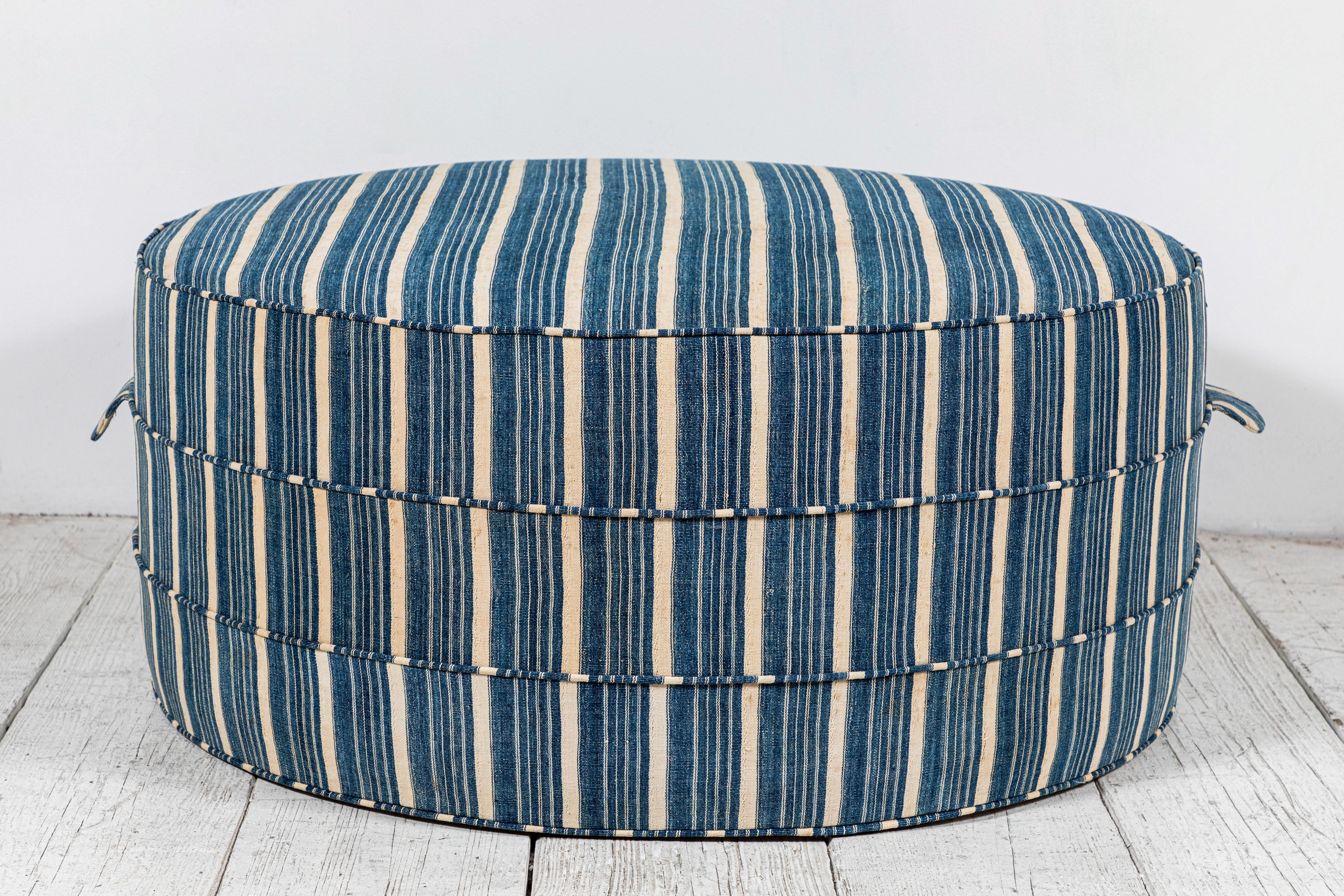 Solid wood frame and upholstered hassock with two ring piping and double handle details offers versatility in accent seating. This custom Nickey Kehoe Collection round ottoman is upholstered in vintage African striped Indigo from Burkina Faso.