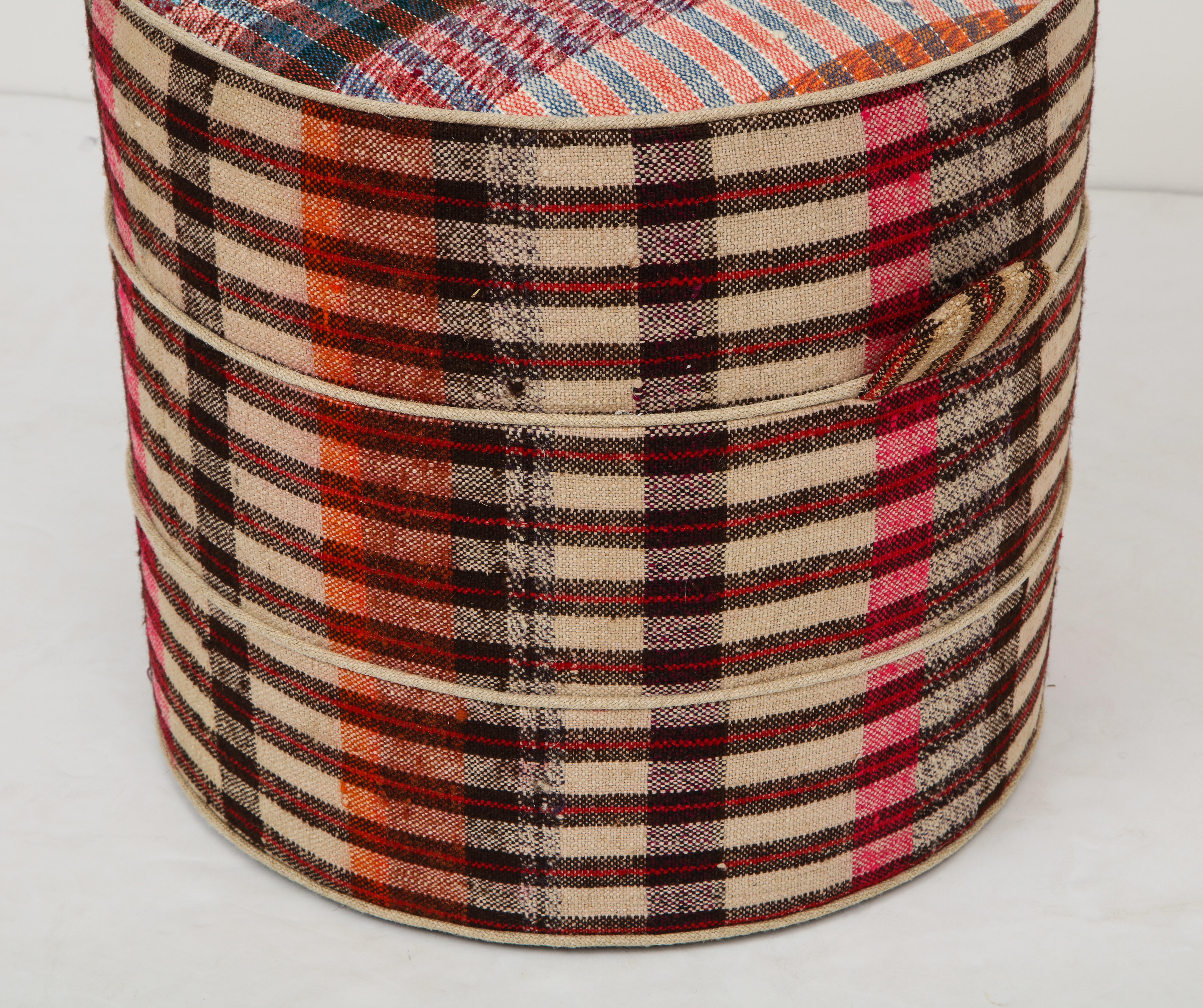 The Nickey Kehoe small round hassock boasts a solid wood frame and beautiful two ring piping details and handles. The piece is one-of-a-kind and upholstered in a vintage French plaid fabric.