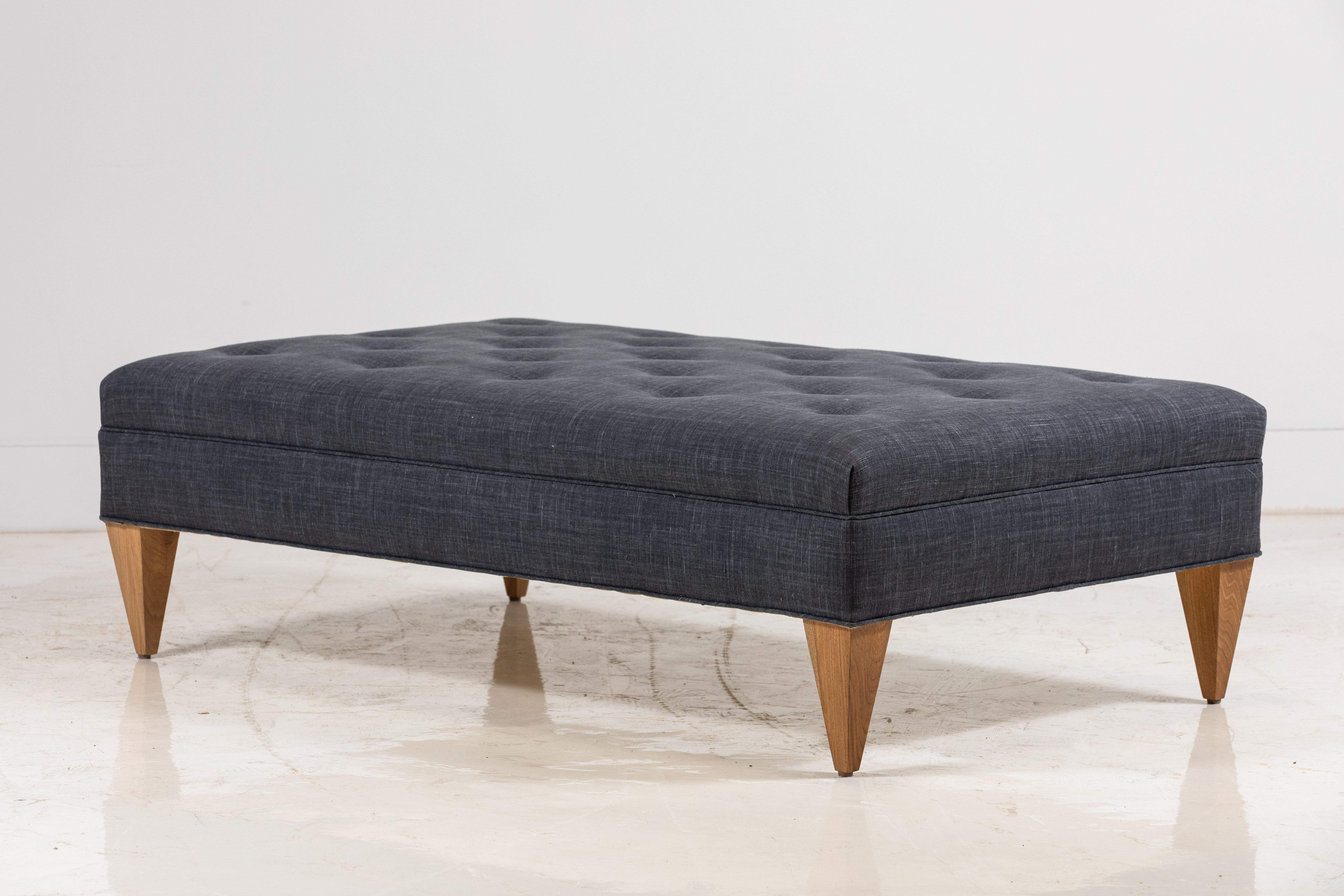 Nickey Kehoe collection tufted ottoman upholstered in a Gunmetal Libeco Linen. The ottoman is finished with tapered natural oak legs.