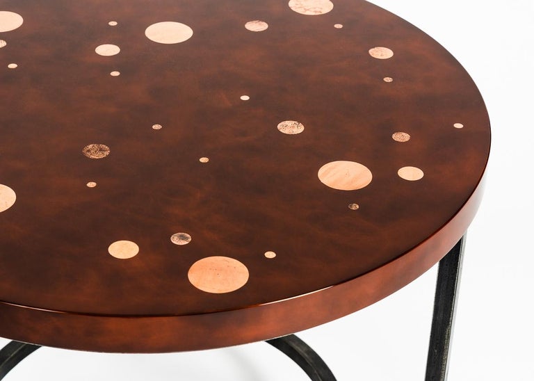 This exquisite occasional table is well named -- the celestial intimated in the perfectly round top, circular copper leaf details, and the patinated steel base which echoes both. The table, with its rich, red lacquer top, versatile size, and elegant