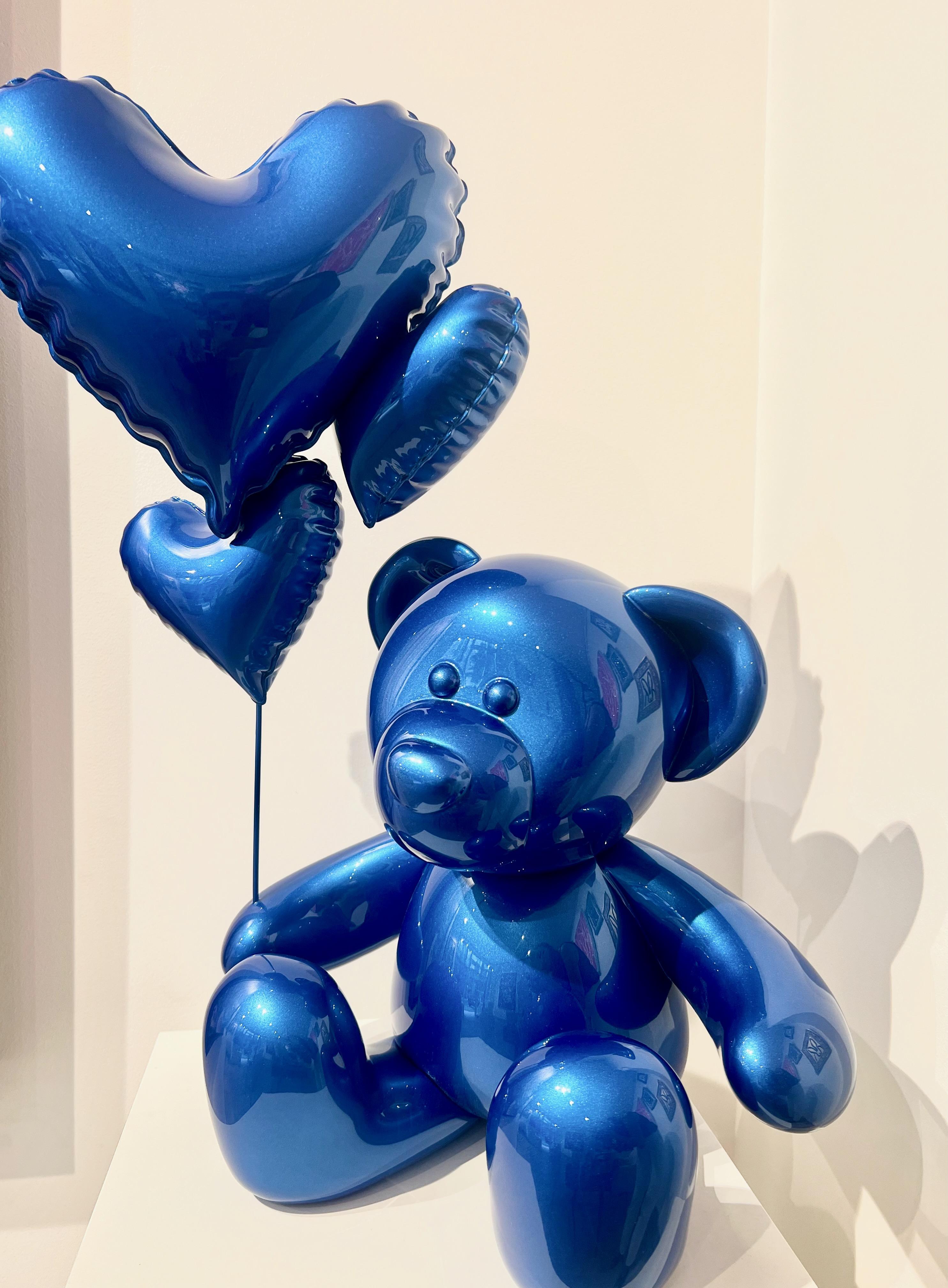 This captivating artwork features a stylized teddy bear crafted from a shiny material in a striking metallic blue color.

Its smooth, reflective surfaces catch the light in a way that creates a dazzling visual effect. The bear is seated, with its