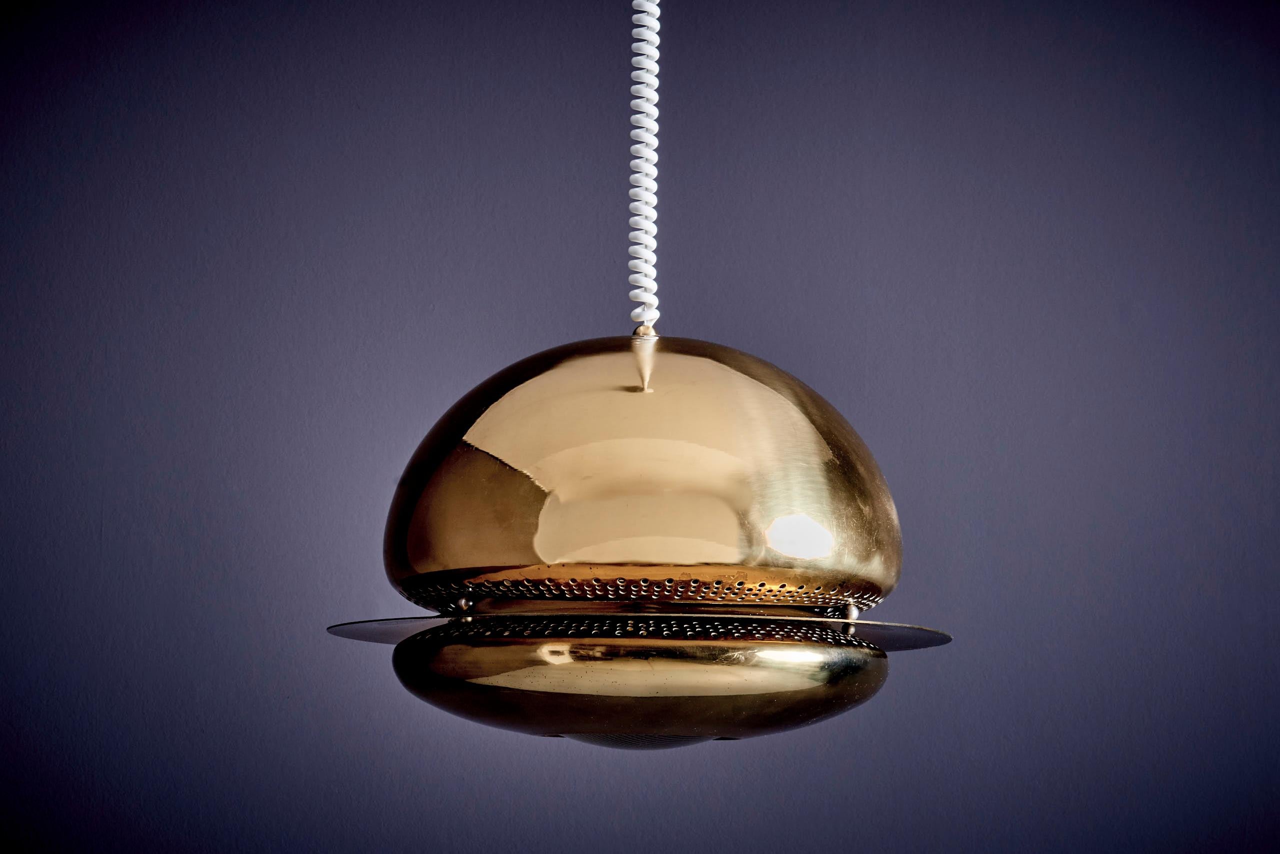 Die Nictea Pendelleuchte besteht aus zwei abgerundeten Teilen, die nahtlos durch sorgfältig integrierte Metallteile verbunden sind, die im Mittelpunkt des Designs stehen. Das Licht dringt sanft durch das perforierte Band zwischen den beiden