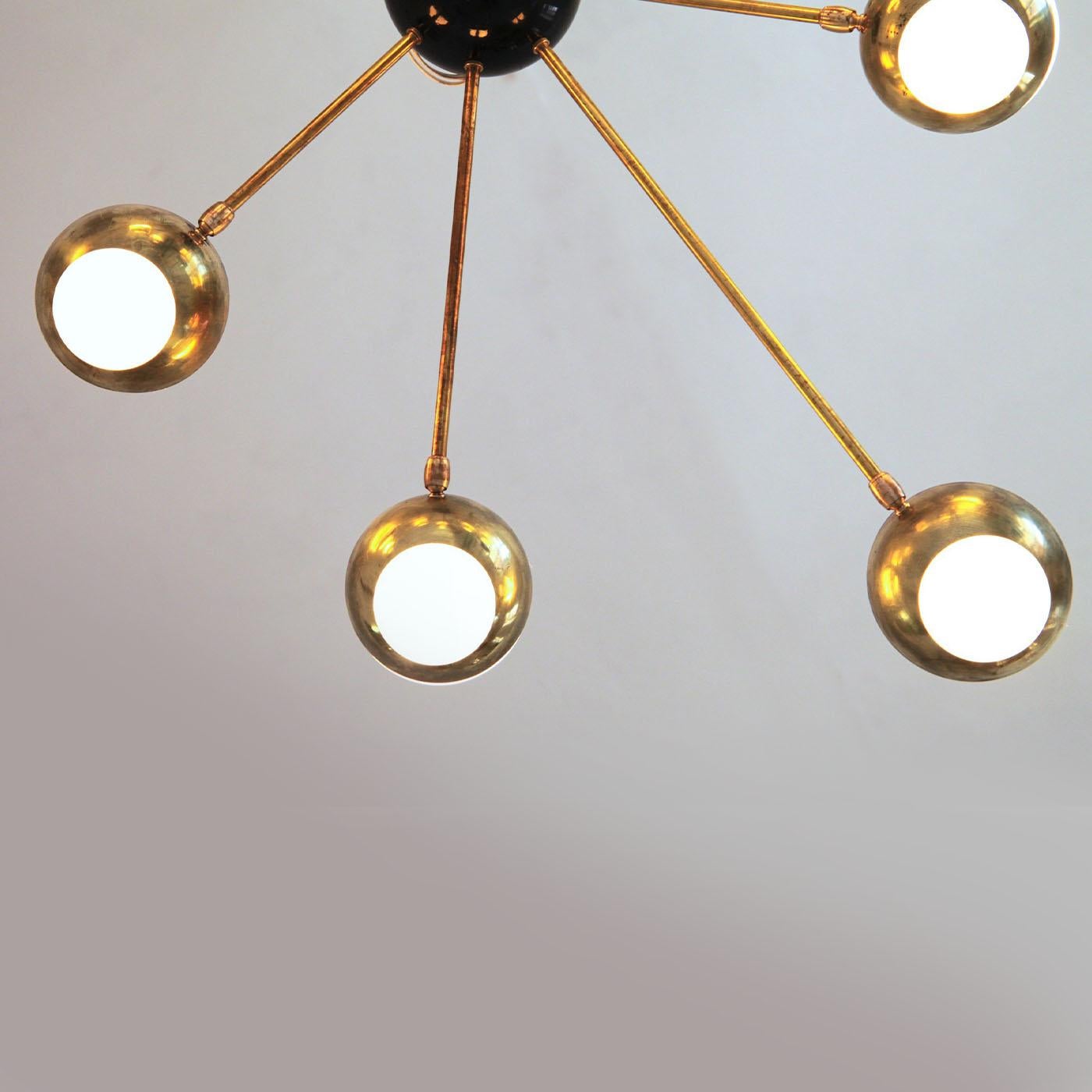 Distinguished by a captivating asymmetrical design with spokes radiating from a black ceiling mount, this precious brass chandelier owes its name (the Italian for nest) to the shape of the pivoting elements welcoming the glass spheres. A patient