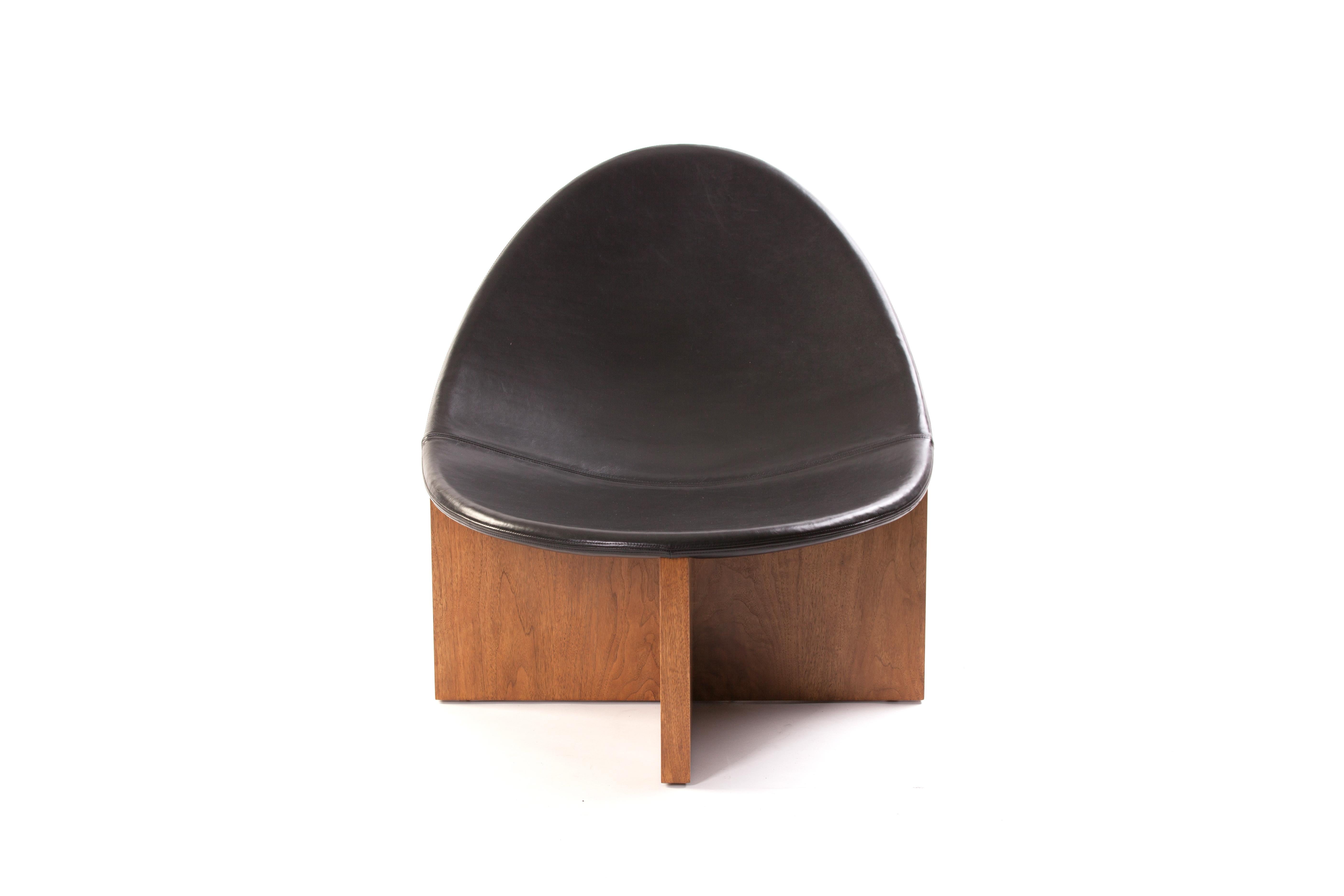 Nido lounge chair with solid walnut base and black leather upholstered seat.The Nido chair was the result of playing with the juxtaposition of shapes. The egg-like shape of the leather upholstered wood seat nesting in the cross shaped solid wood