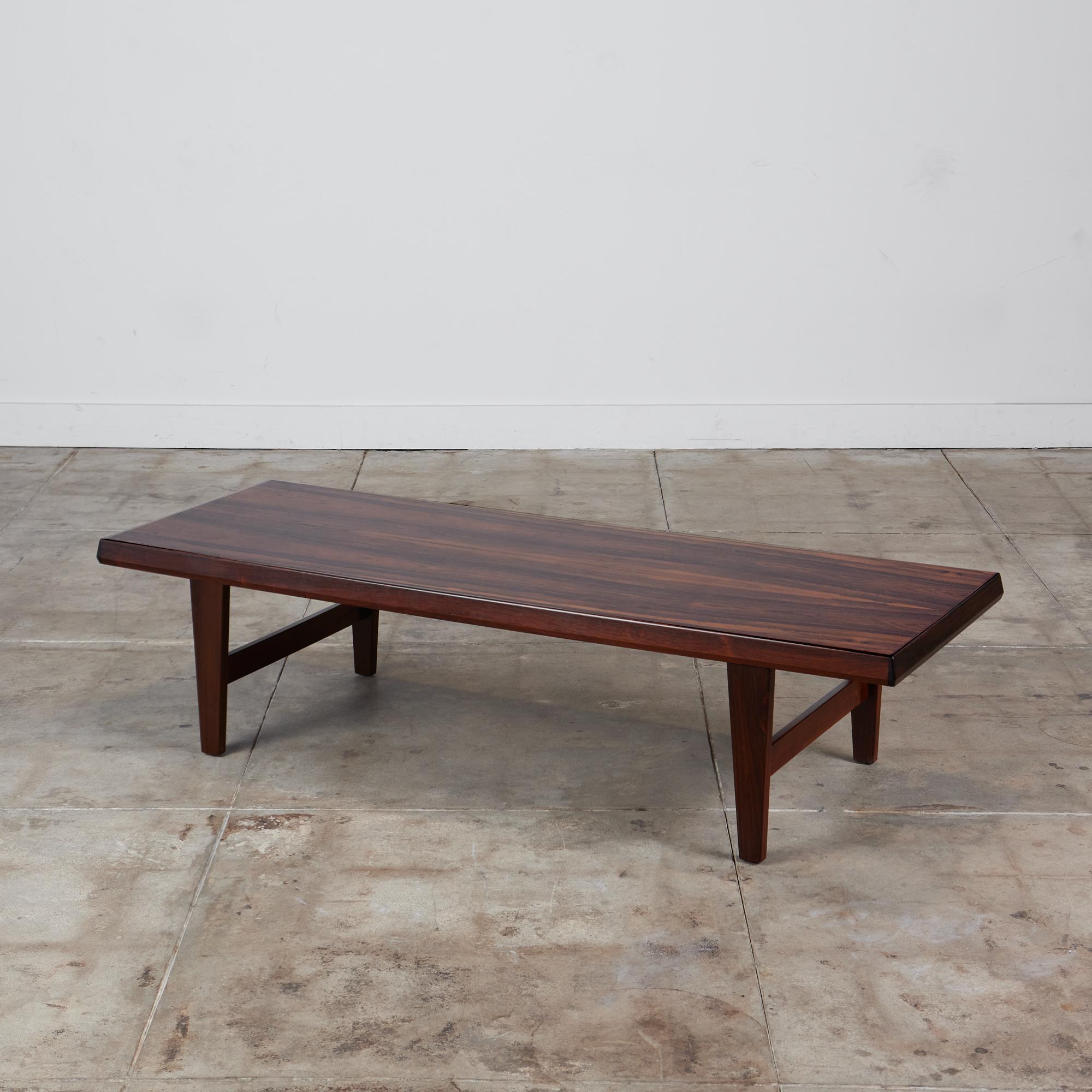 A generously proportioned, coffee table in highly figured Brazilian Rosewood by Niels Bach, a manufacturer based in Randers, Denmark. The long tabletop has angled edges and is thick enough for the piece to double as a bench. The table is supported