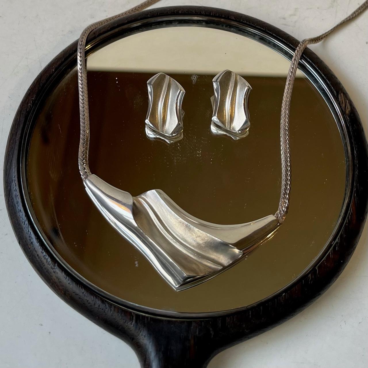 A late 1960s or early 1970s pendant necklace with matching earrings/ear-clips by Danish silversmith N. E. From. The set exhibits a delicate texture/polish to its abstract shapes. The pendant comes with its original 40 cm integrated Bismarck necklace