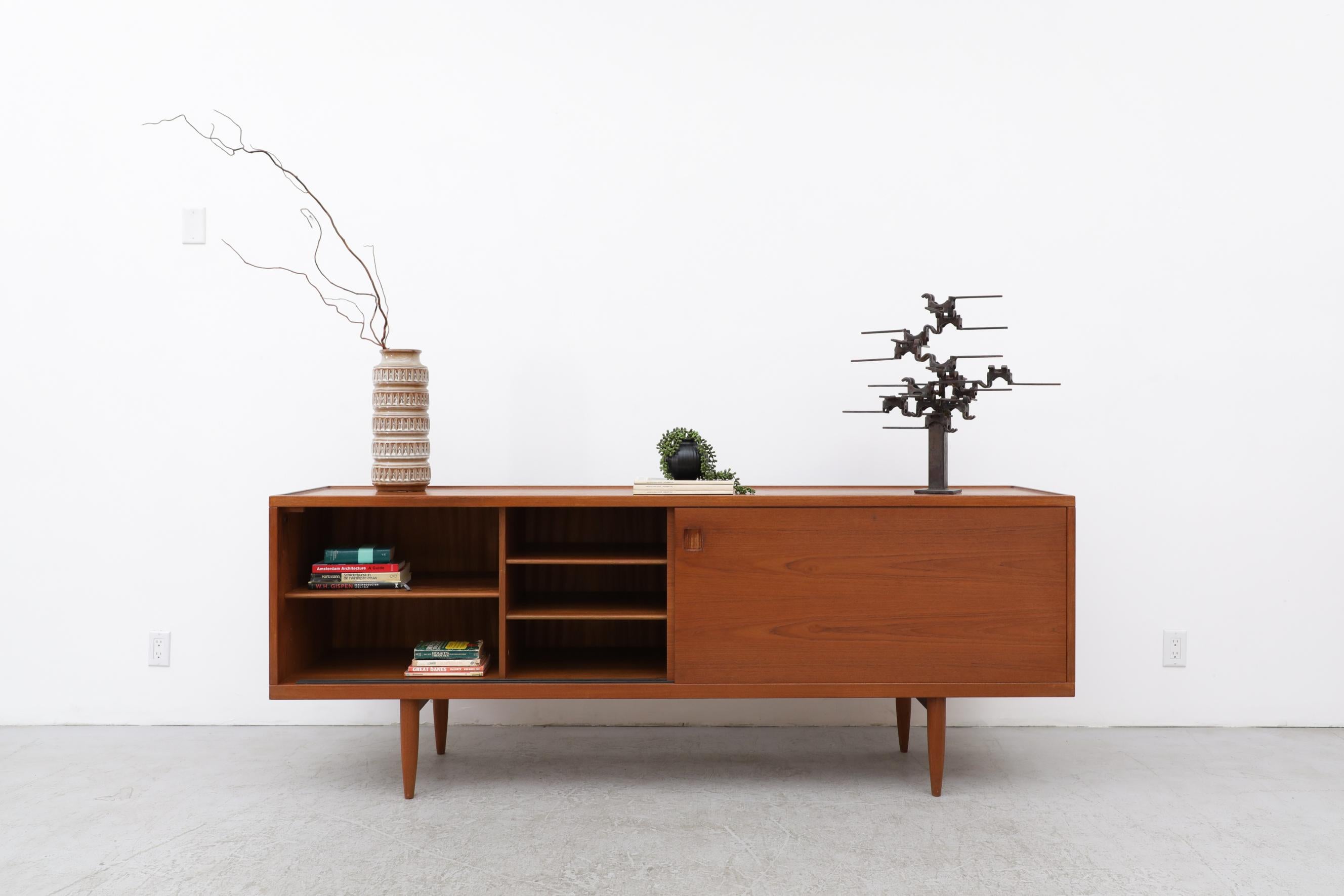 Mid-Century Danish Teak sideboard, Model 20, designed by Niels Moller, 1960's. This sideboard has double sliding doors with matchbook grain. The doors have inset square carved pulls that hide shelving on one side and 2 compartments on the right, one