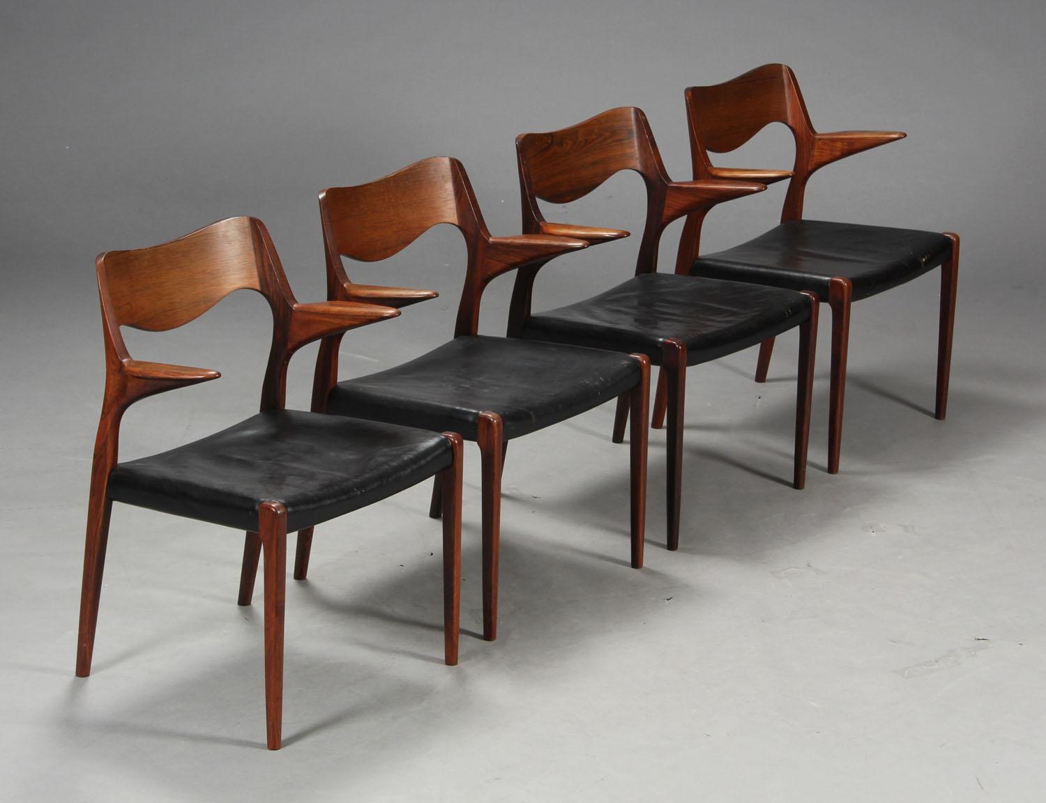 Priced and sold as single chairs, pictured is a set of four dining chairs with arms designed by Niels Otto Moller in 1951 and made by JL Moller before 1969, as indicated by the round disc label. Original black leather is in fair condition showing