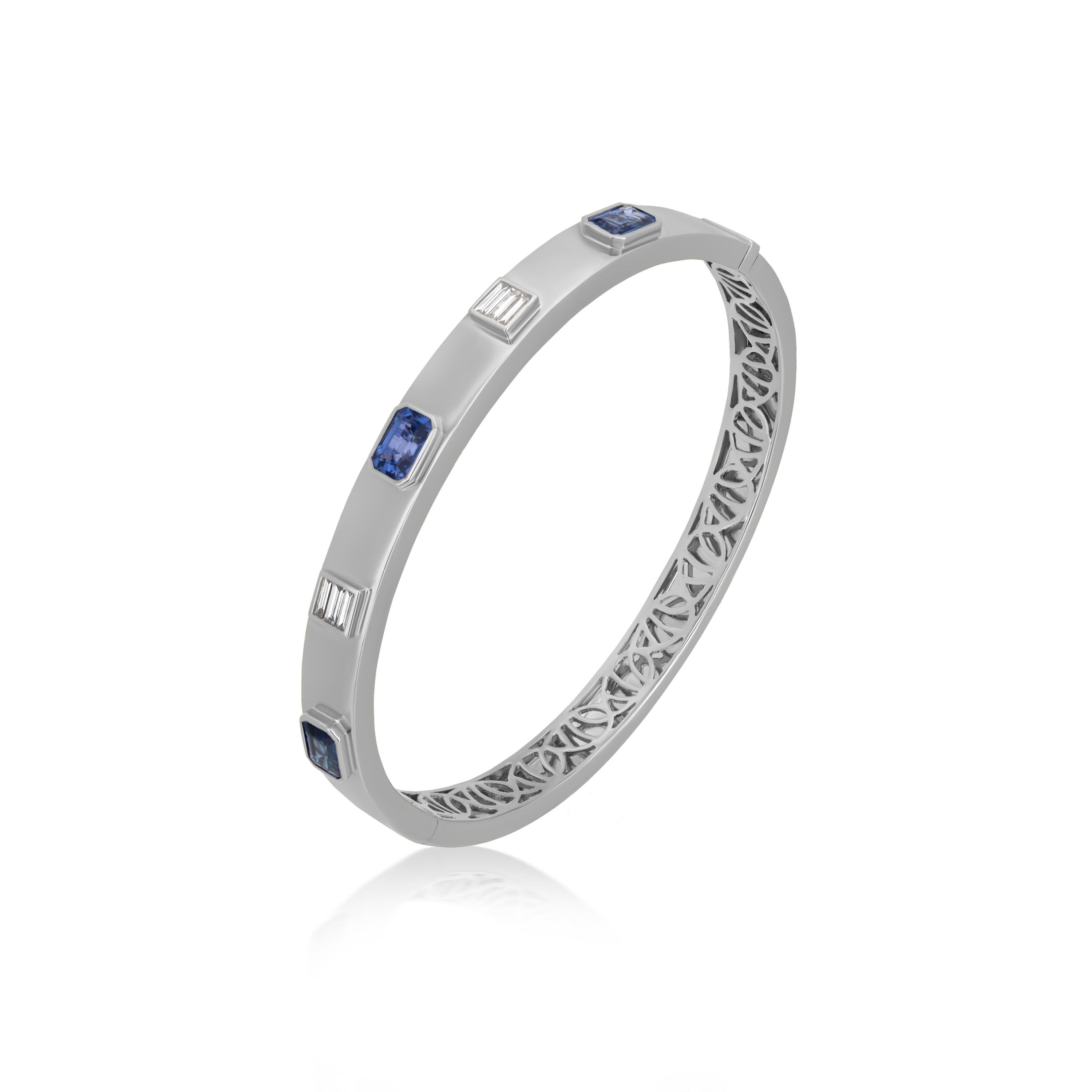 This blue sapphire bangle is beautified by Nigaam with baguette full-cut white diamonds and octagon-shaped blue sapphires encrusted on 18K White Gold. The white diamonds are in the bar setting and the blue sapphire in a bezel setting, lending the
