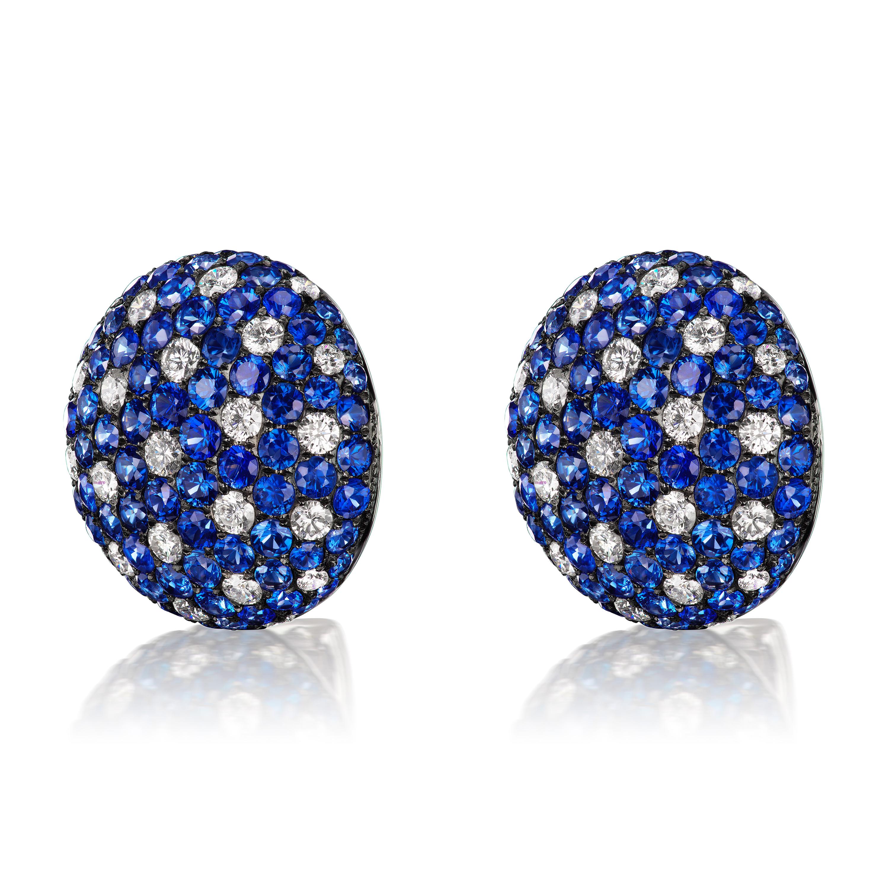 The gorgeous stud earring created by Nigaam in a stunning circle frame made of 18 karat white gold plated in black rhodium and set with a 7.84 carat round blue sapphire and a 2.01 carat round diamond. The earring's overall appeal is enhanced by its