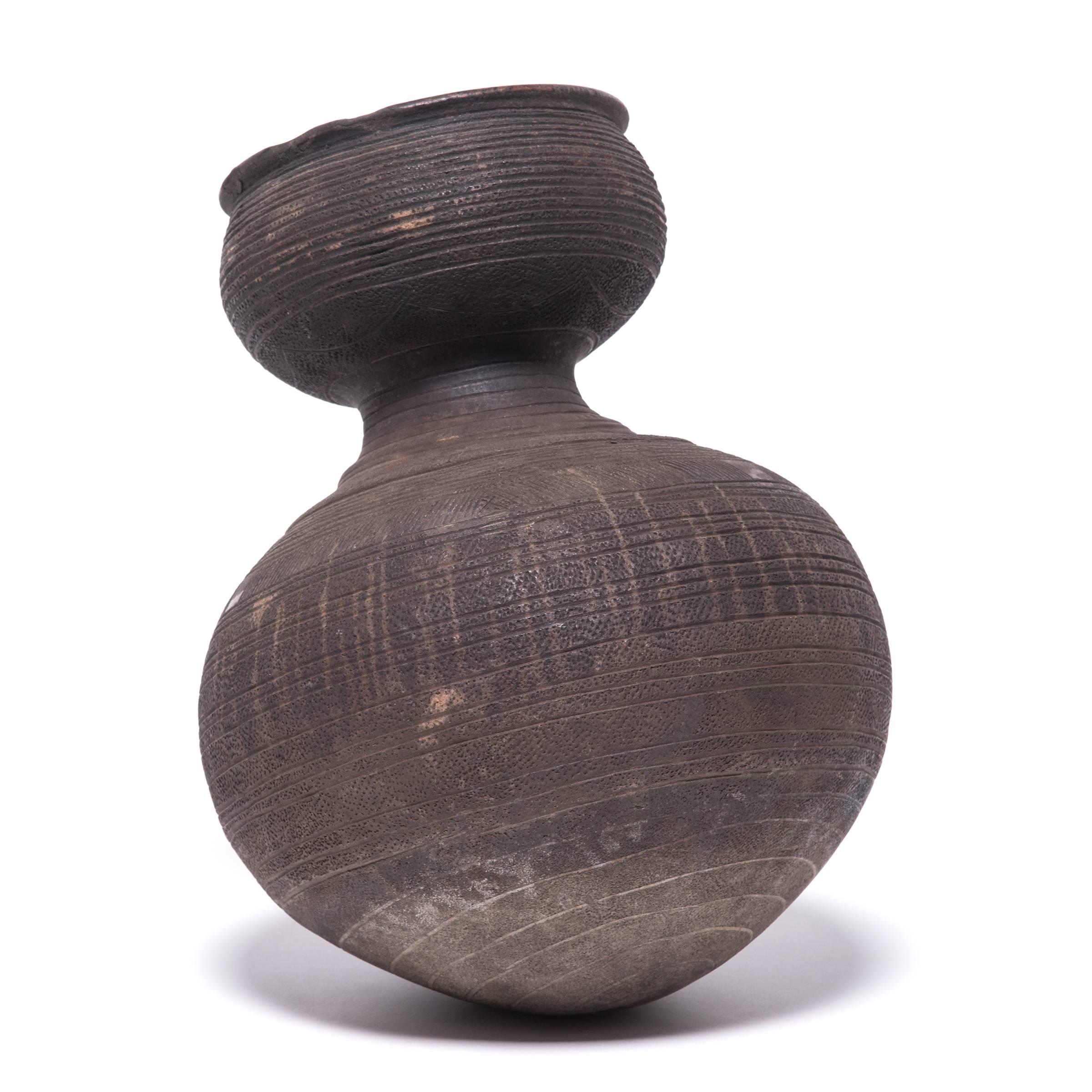 Inspired by the natural world, Nupe ceramicists fired this water vessel in the shape of a gourd. The vessel's varied textures and colors come from its functional design. The dimpling and geometric markings were engraved to give the drinker a better