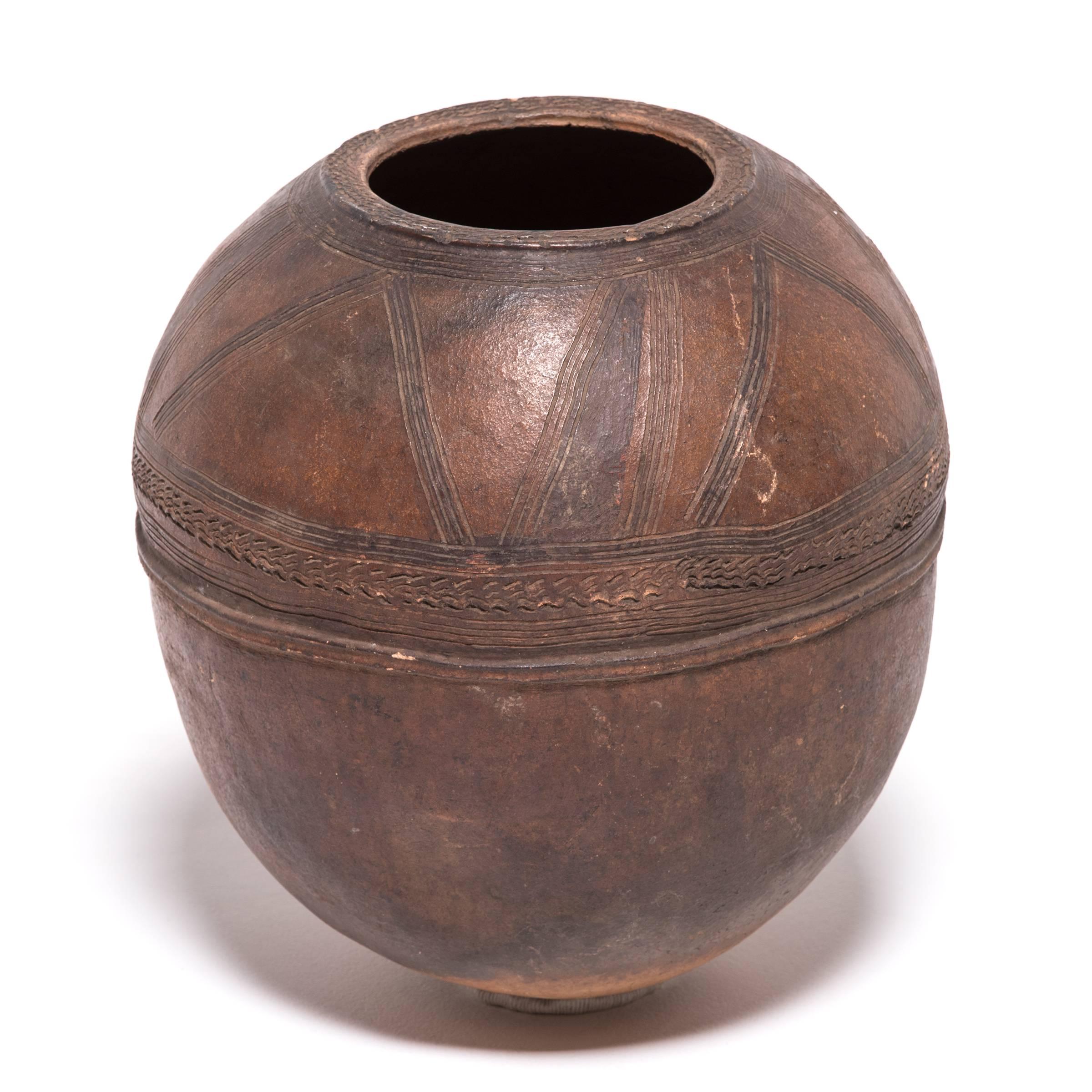 Elegantly embellished with geometric designs, this rounded water vessel is a fine example of Nupe ceramics. The vessel's many textures are not only decorative, they are also integral part of its functional design. The patterns and bands were etched