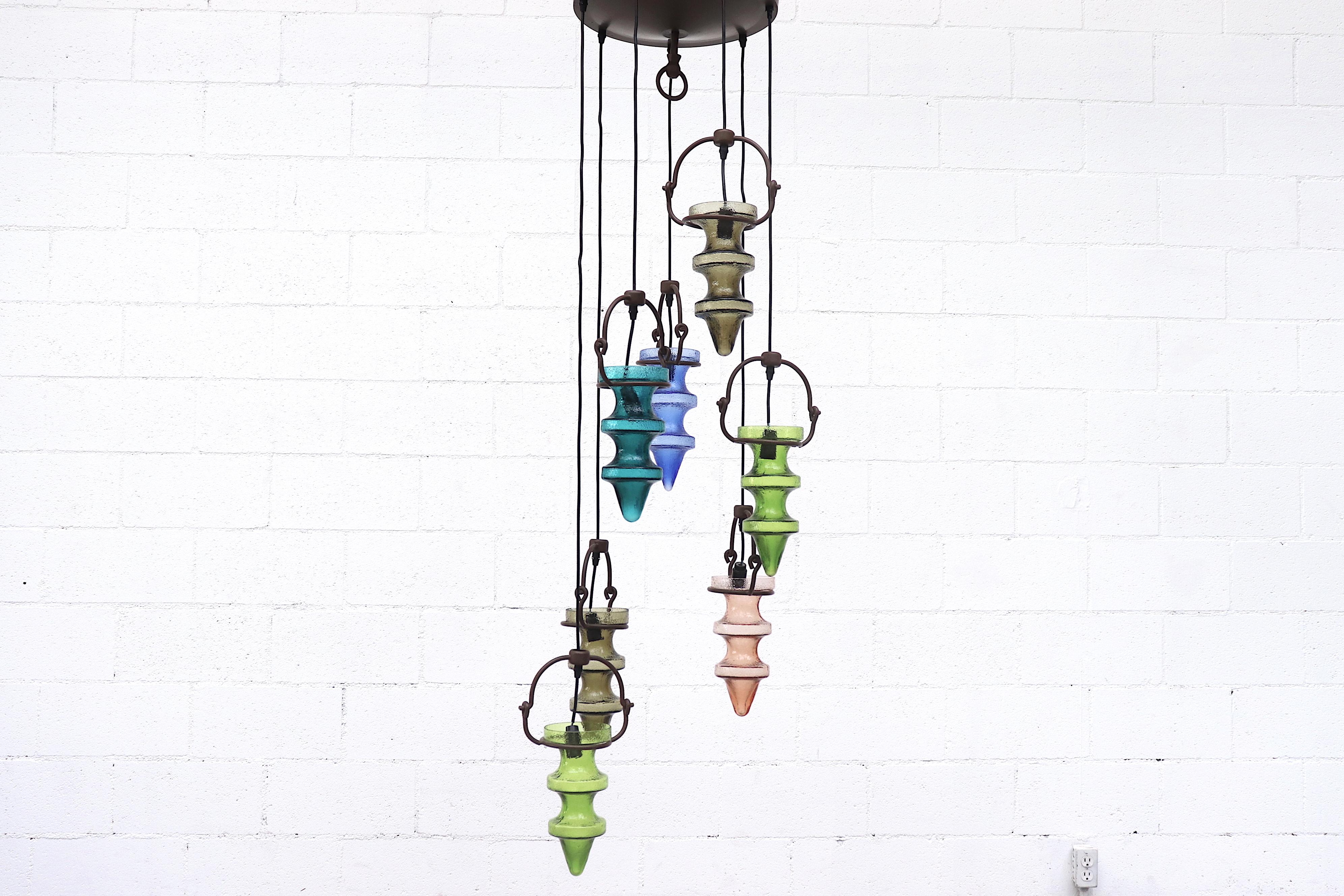 Beautiful, multicolored, mid century chandelier consisting of stalactite glass shades that hang from brown enameled forged iron hanging cradles. Designed by Finnish designer Nanny Still McKinney and produced by the Val Saint Lambert Glass Factory