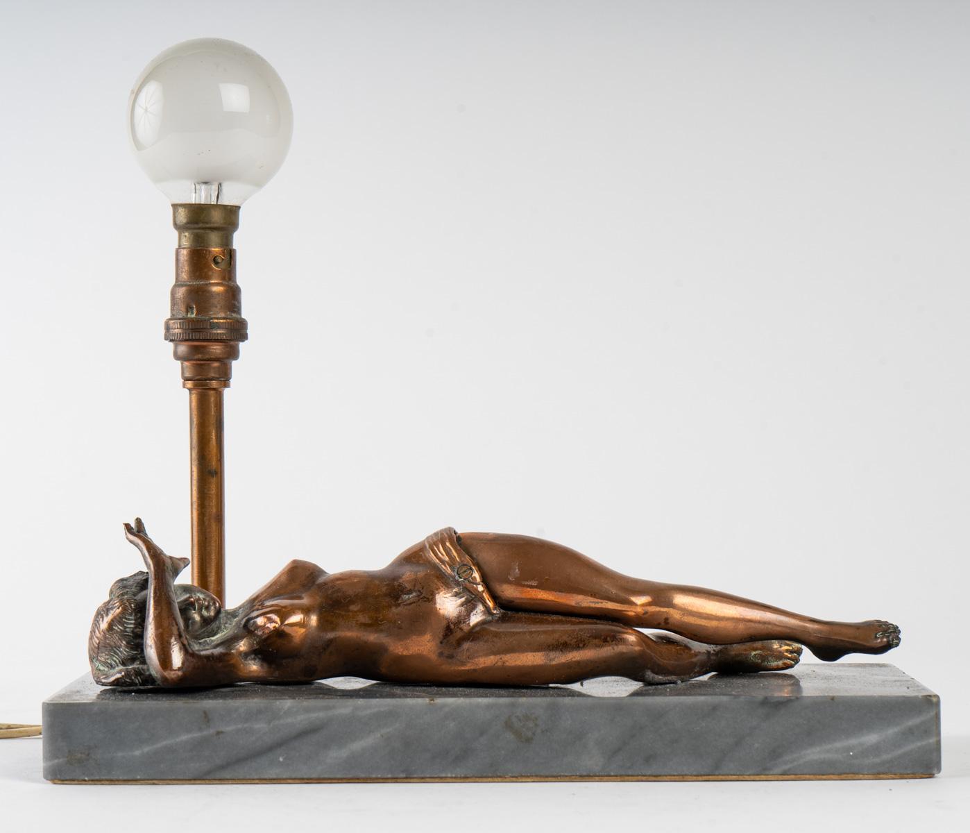 Nightlight, cigar cutter table Lamp depicting a young woman with her left leg rising to cut a cigar, bronze and marble, early 20th century, 1920.
Measures: H 20 cm, W 22 cm, D 9 cm.