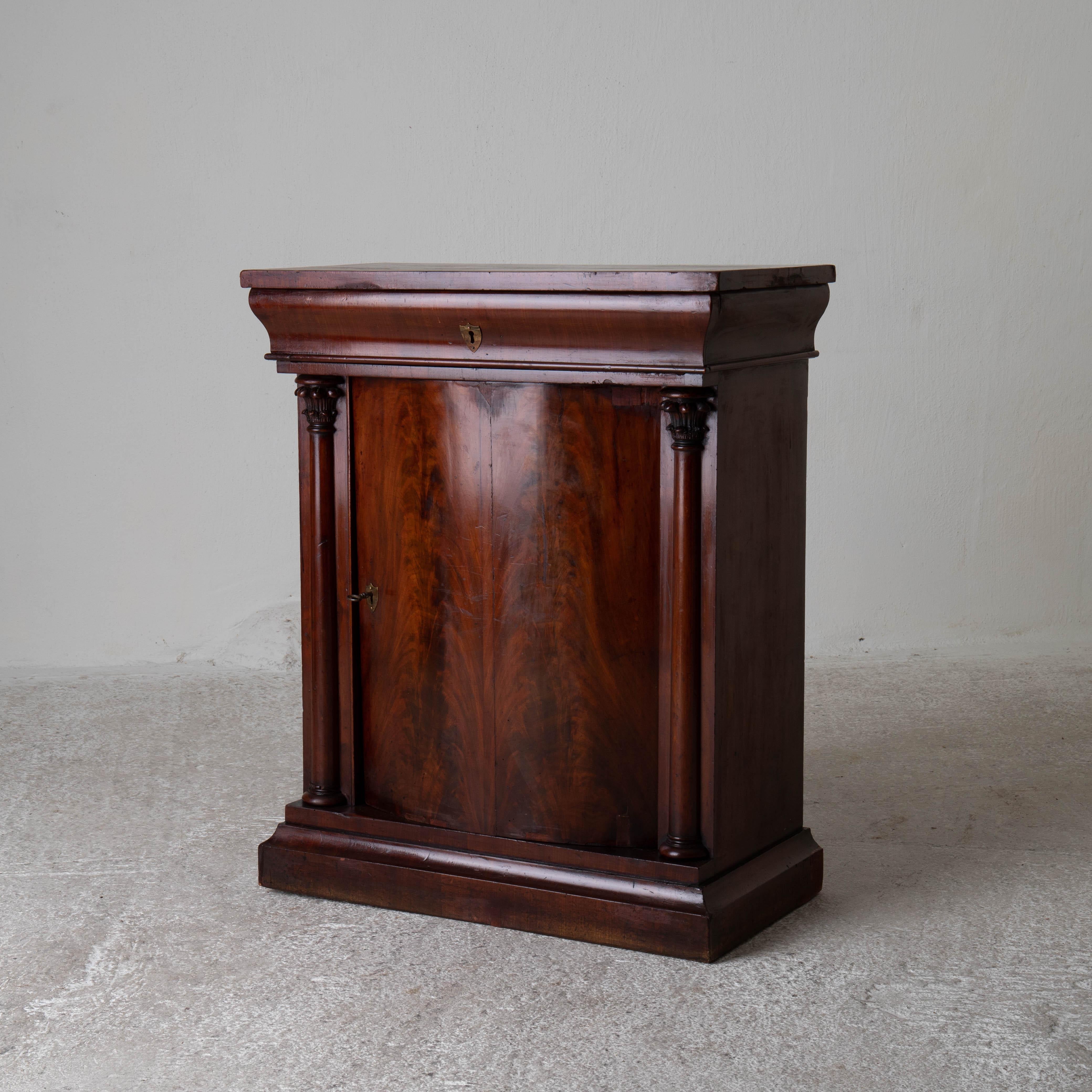 Nightstand side table Swedish mahogany 19th century neoclassical Sweden. A nightstand or side table in dark brown mahogany made during the Karl Johan Period 1810-1830 in Sweden. Curved door with a shelf interior. Drawers below the top. Column shaped