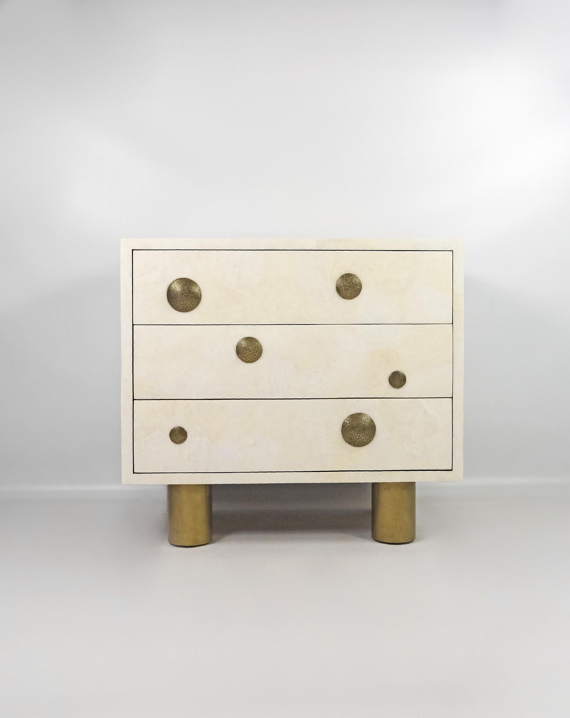 The bedside table is made of white rock crystal marquetry with a polished satin finish.
It has 3 drawers on push to open rails, with casted bronze decors. 
The nightstands seats on four cylinder legs finished with an antic brass patina.

The
