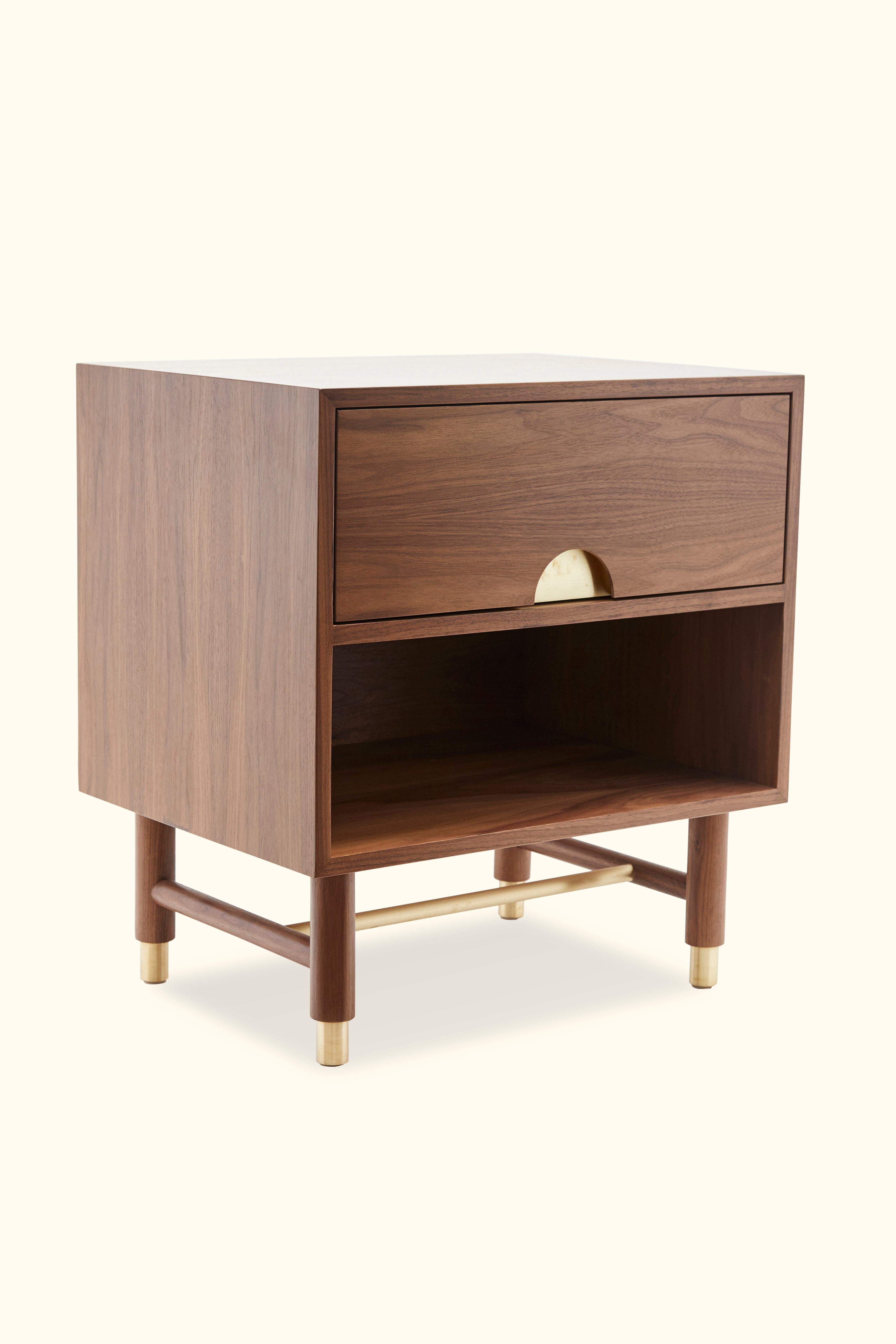 The Niguel side table features one drawer and an open shelf. Details include leveling brass cap feet, a brass stretcher on the base, lacquered interior and inset brass hardware. Available in American walnut or white oak. Shown here in  Light Walnut.