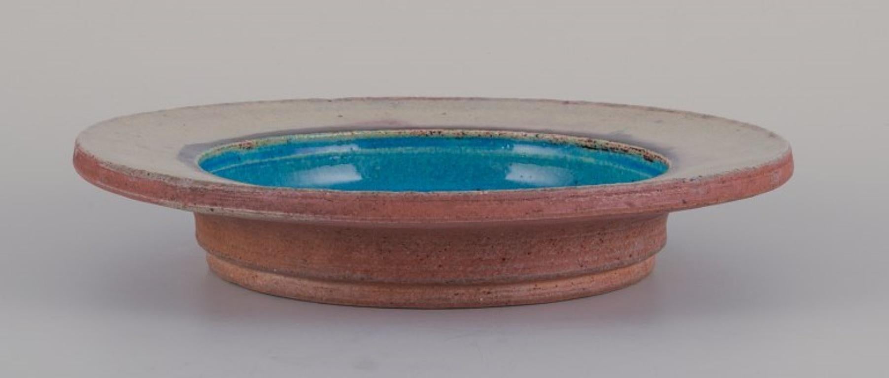 Nils Joakim Kähler (1906-1979) für Kähler, Dänemark. 
Runde Keramikschale im modernistischen Stil. Türkisfarbene und cremefarbene Glasur.
Ungefähr in den 1960er Jahren.
Markiert.
In perfektem Zustand.
Abmessungen: Durchmesser 26,5 cm x Höhe 4,7