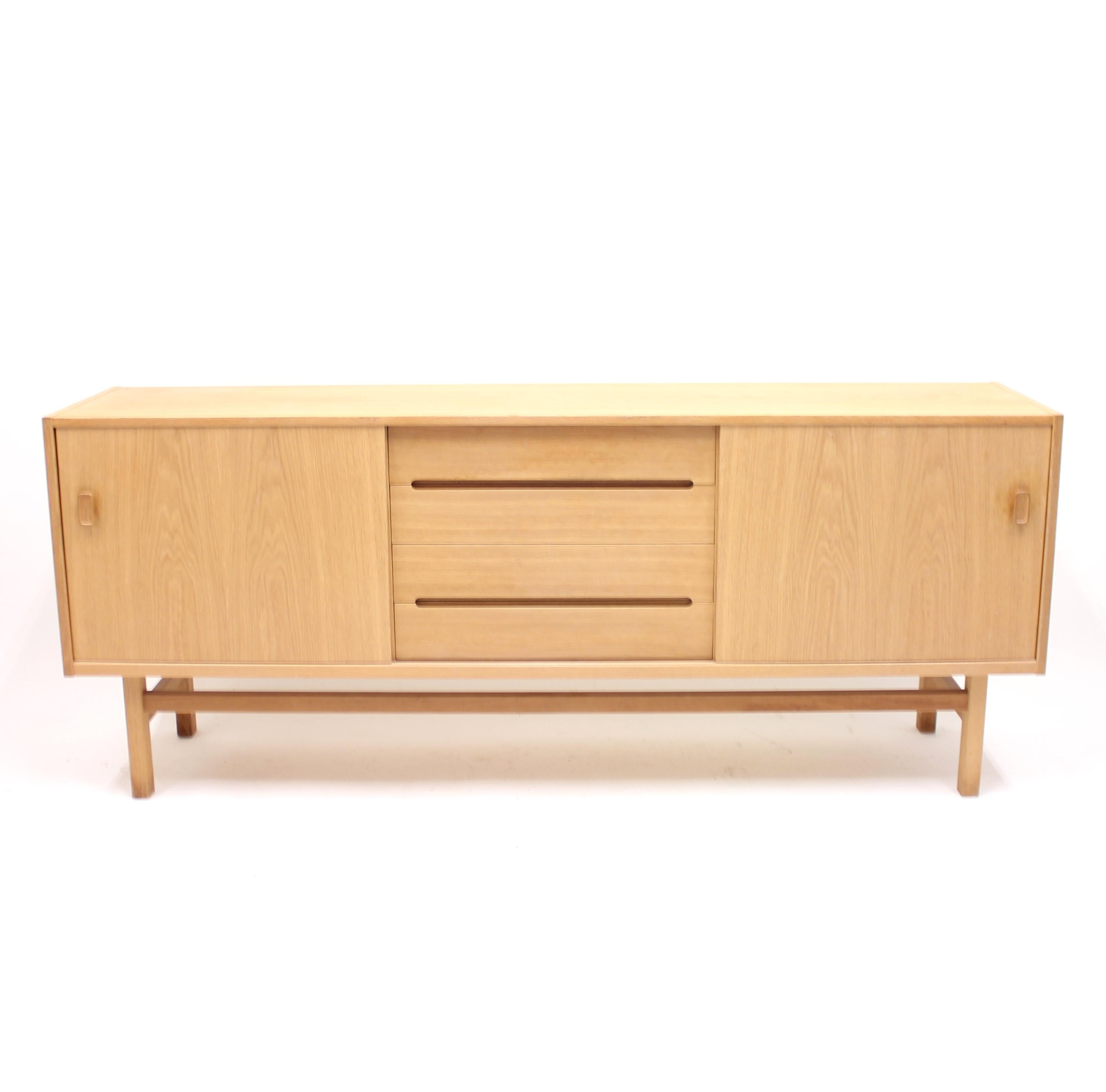Oak sideboard, model Arild, designed by Nils Jonsson for Swedish manufacturer Troeds. Middle section with four drawers. The top drawer contains compartments for cutlery and a movable tray. All clad in a blue felt fabric. Both sides with sliding
