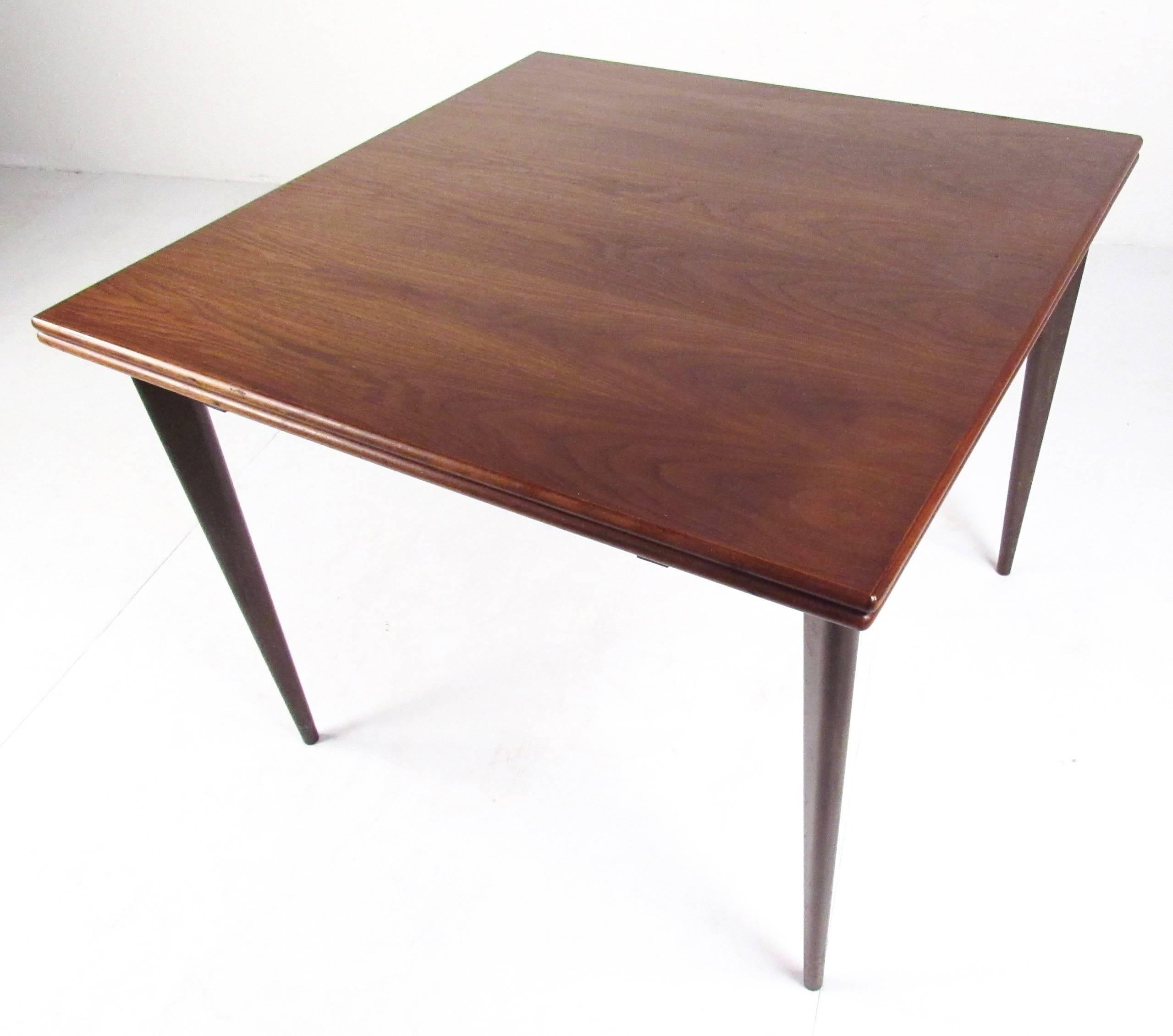 This stylish Mid-Century Modern dining table by Nils Jonsson is perfect for kitchen, dining room, or apartment use. Versatile design allows this 35.5 inch square table to open up to a width of 71 inches. Rich wood grain top is accented by brass