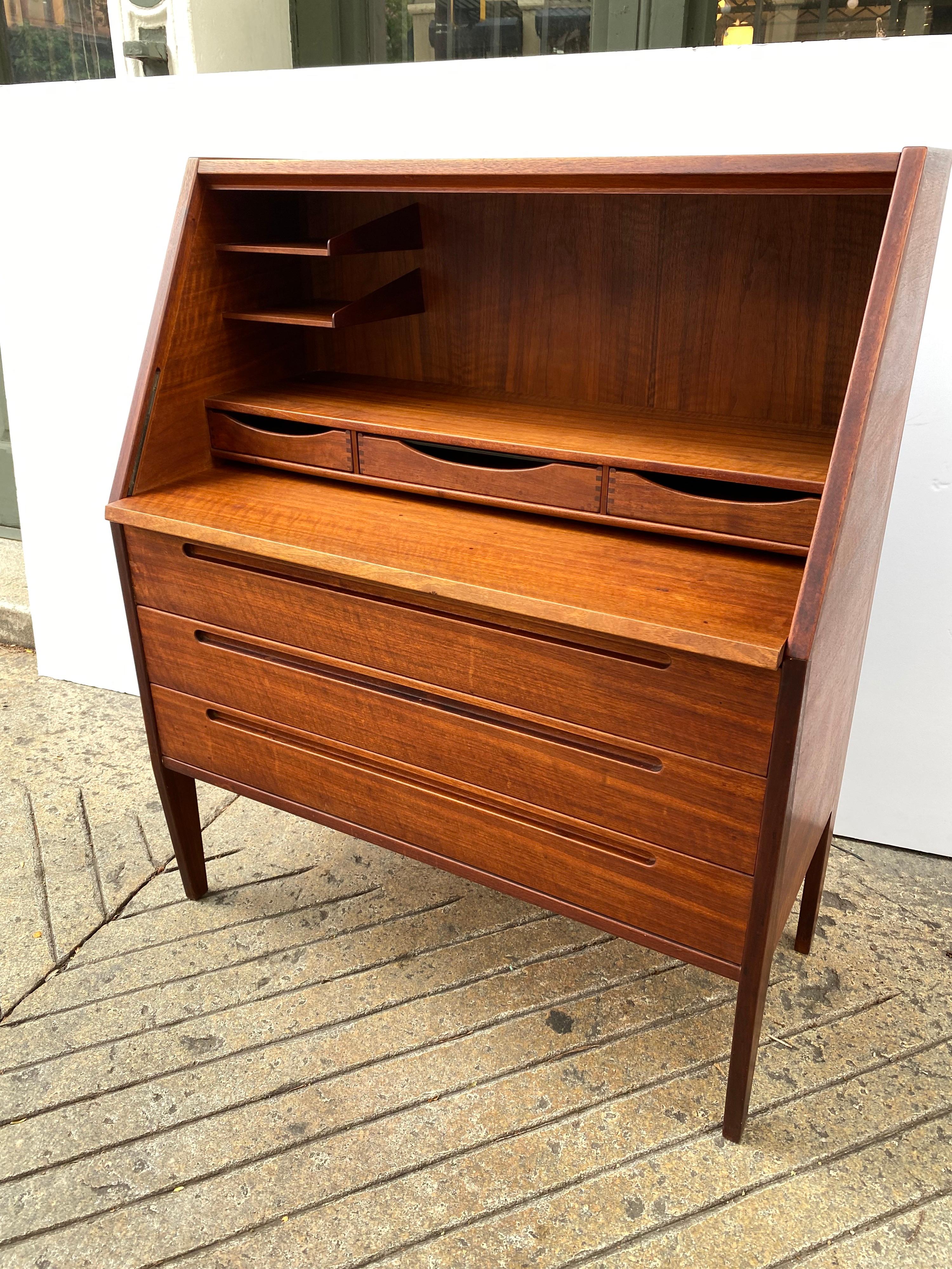 Nils Jonsson teak desk. Front Drops forward and pulls out to give you ample writing surface. Beautifully made with dove-tailed joints on all drawers and recessed drawer handles. Sides show a great design with tapering legs. Inside their are two