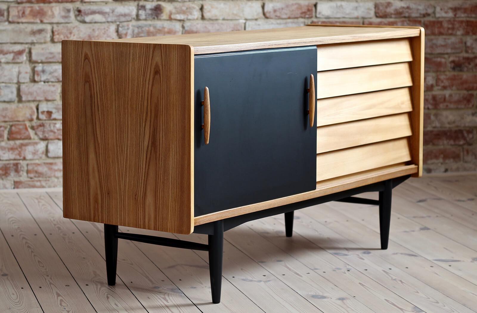 This is a not so common model of sideboard by Nils Jonsson in ashwood with black sliding door, two sculpted handles, elegant black base completed with subtle sculpted legs - a great example of Scandinavian Modern style in its best. The piece was