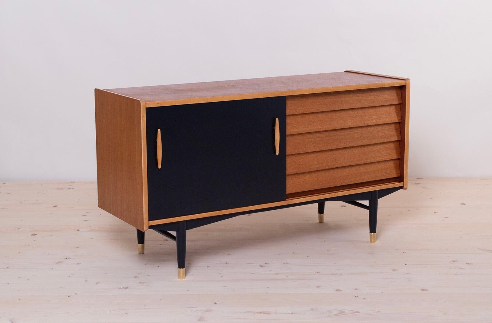 This is not so common model of sideboard by Nils Jonsson in teak wood with black sliding door, a sculpted handle, elegant black base completed with subtle brass legs cups - a great example of Scandinavian Modern style in its best. The piece was