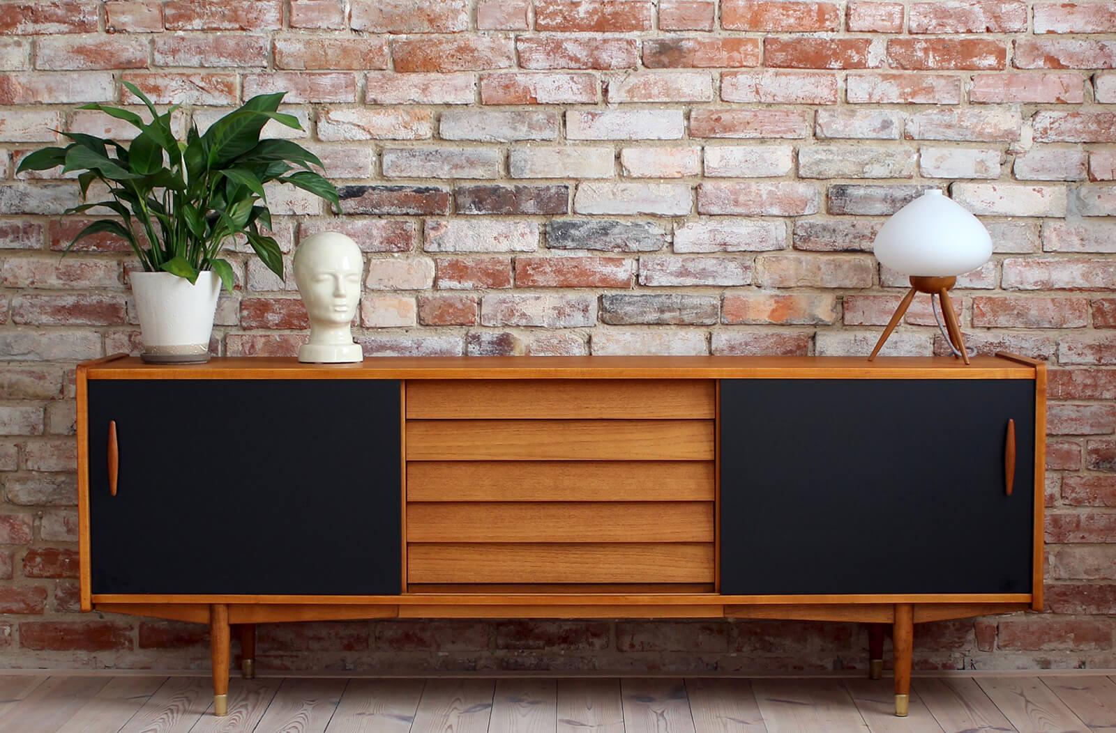 This is not so common model of sideboard by Nils Jonsson in teakwood with black sliding door, two sculpted handles, elegant base completed with subtle sculpted legs, all 4 legs are finished with brass – a great example of Scandinavian Modern style